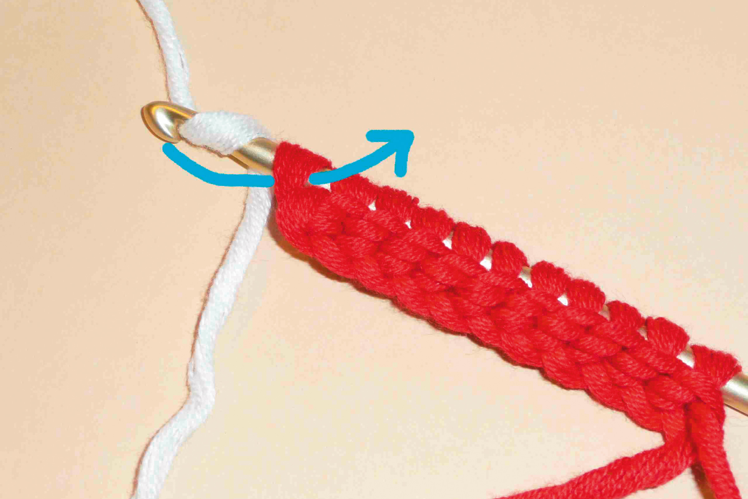 Rote Maschen auf einer goldenen Häkelnadel, kombiniert mit weißem Garn. DIY-Handarbeitsstil.