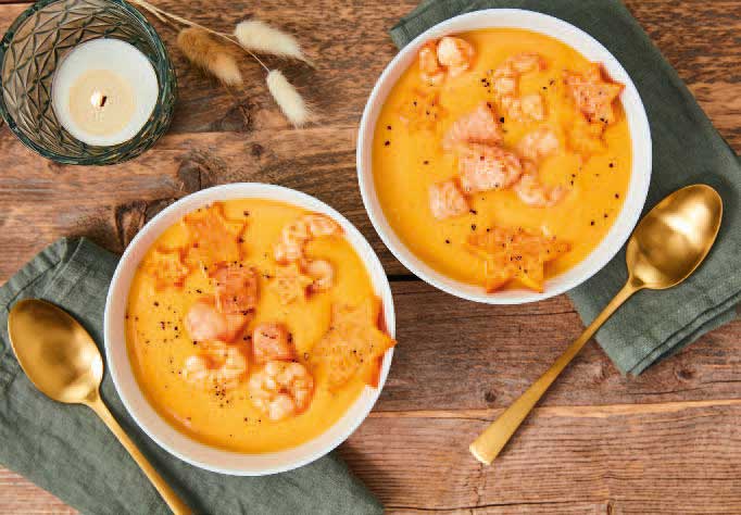 Orangene Suppe mit kreativ geschnittenen Stern-Möhren und Garnelen. Moderne, kunstvolle Präsentation.