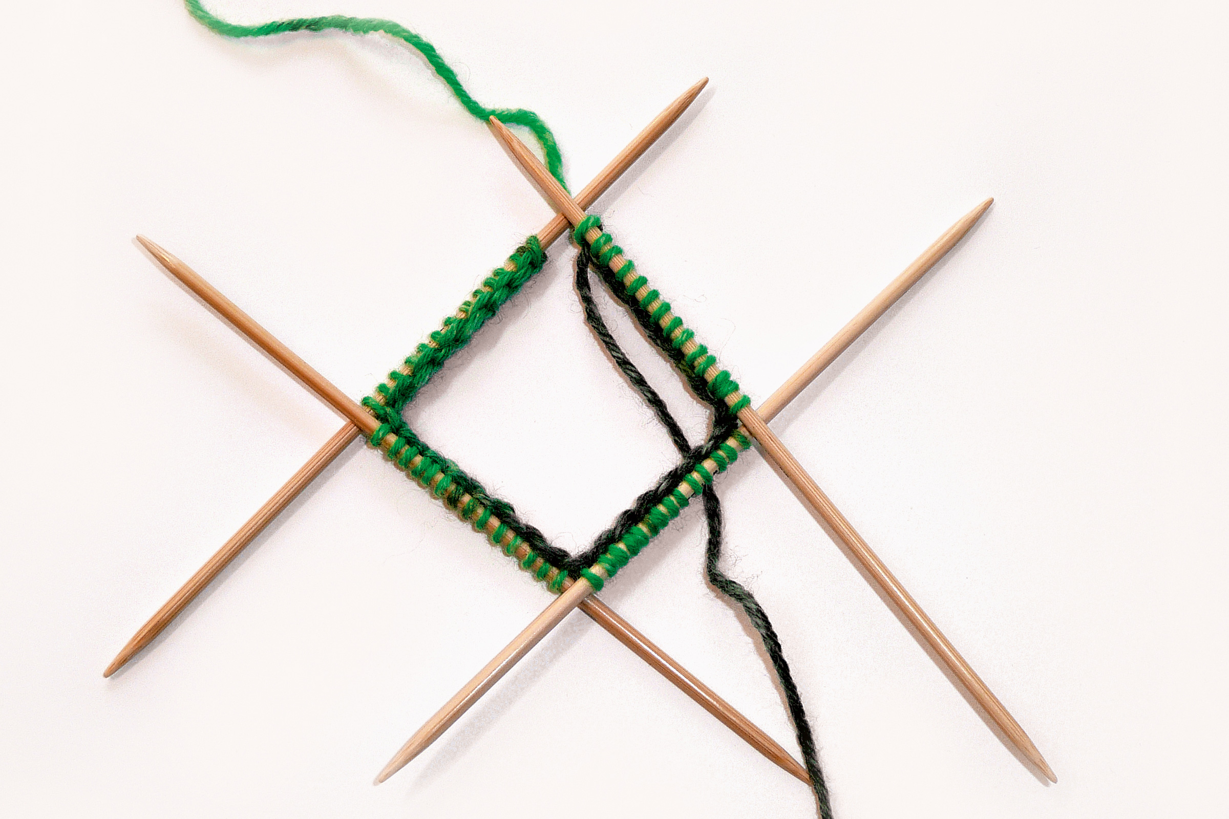 Grünes Strickmuster auf Nadeln, DIY-Handarbeit, modisch und einzigartig gestaltet.
