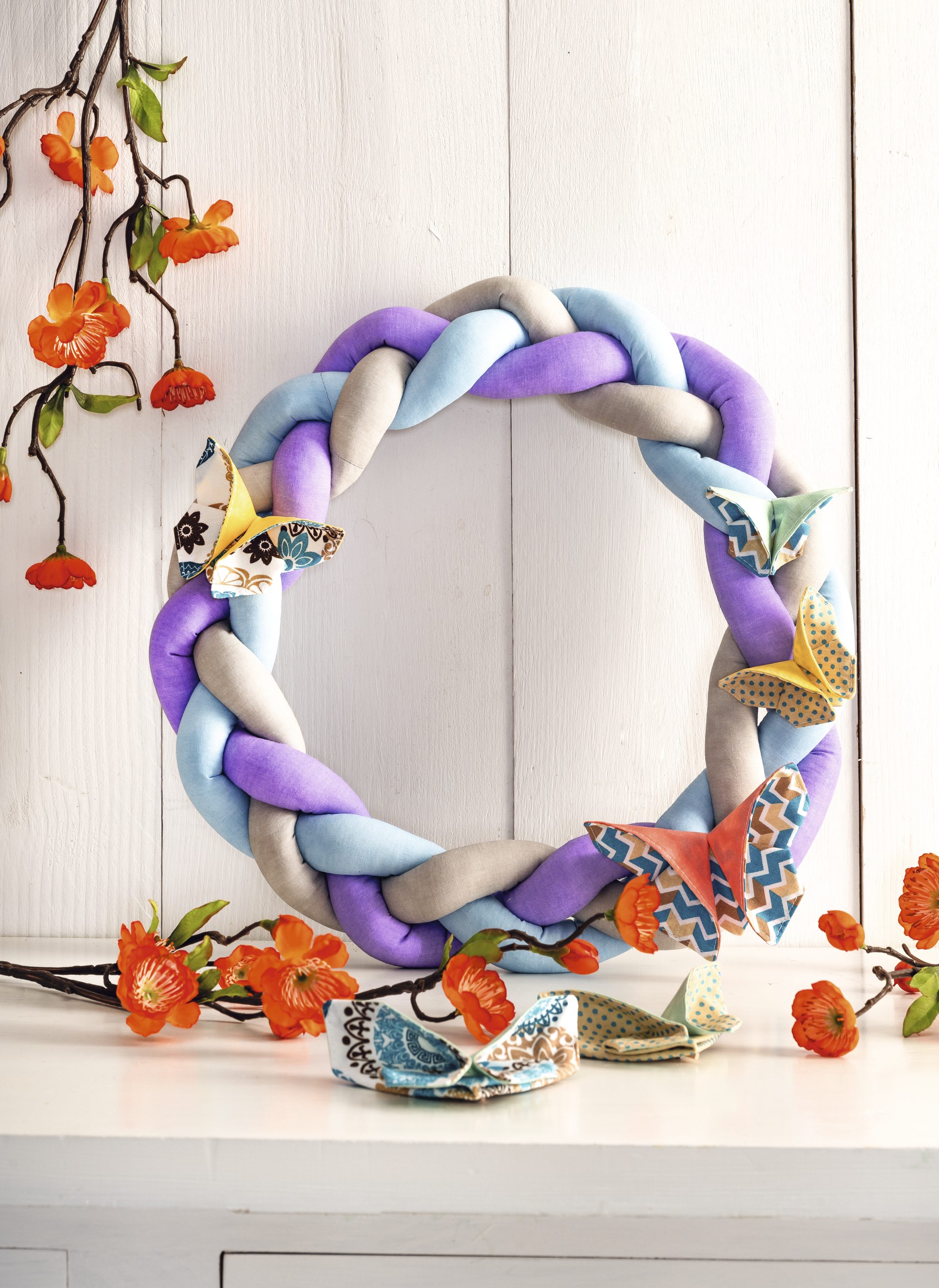 DIY Kranz in Pastellfarben, geflochten, mit bunten Stoffschmetterlingen verziert.