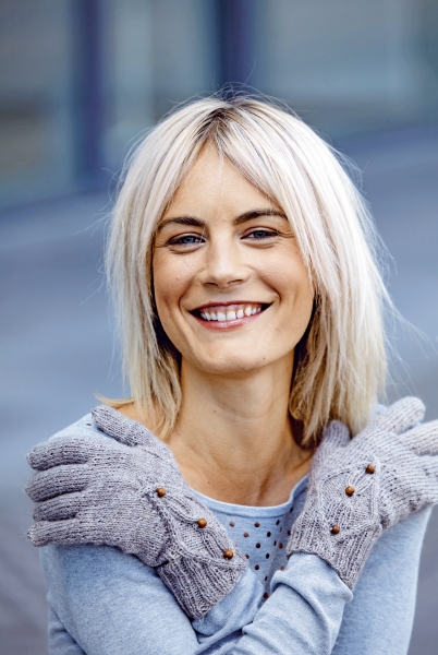 Graue, gestrickte Handschuhe mit Knöpfen, kombiniert mit einem blauen Oberteil. Elegant und handgefertigt.