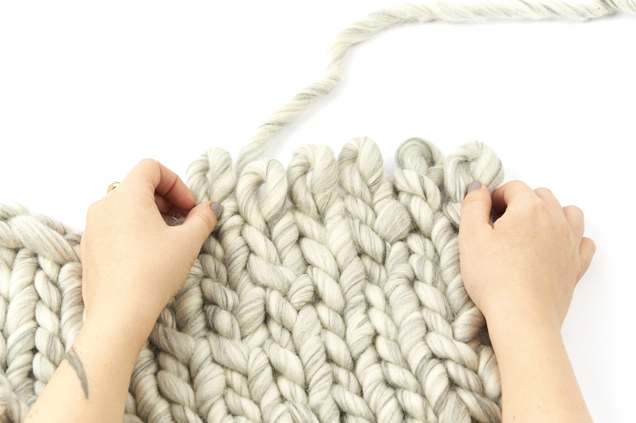 Grobe, hellgraue Strickmaschen, handgemacht, DIY-Stil. Trendige, voluminöse Textur, ideal für modische Accessoires.