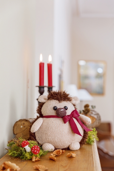 Selbstgemachter Igel aus Wolle, beige und braun, mit roter Schleife. Weiches, gestricktes Design und liebevolle Details.