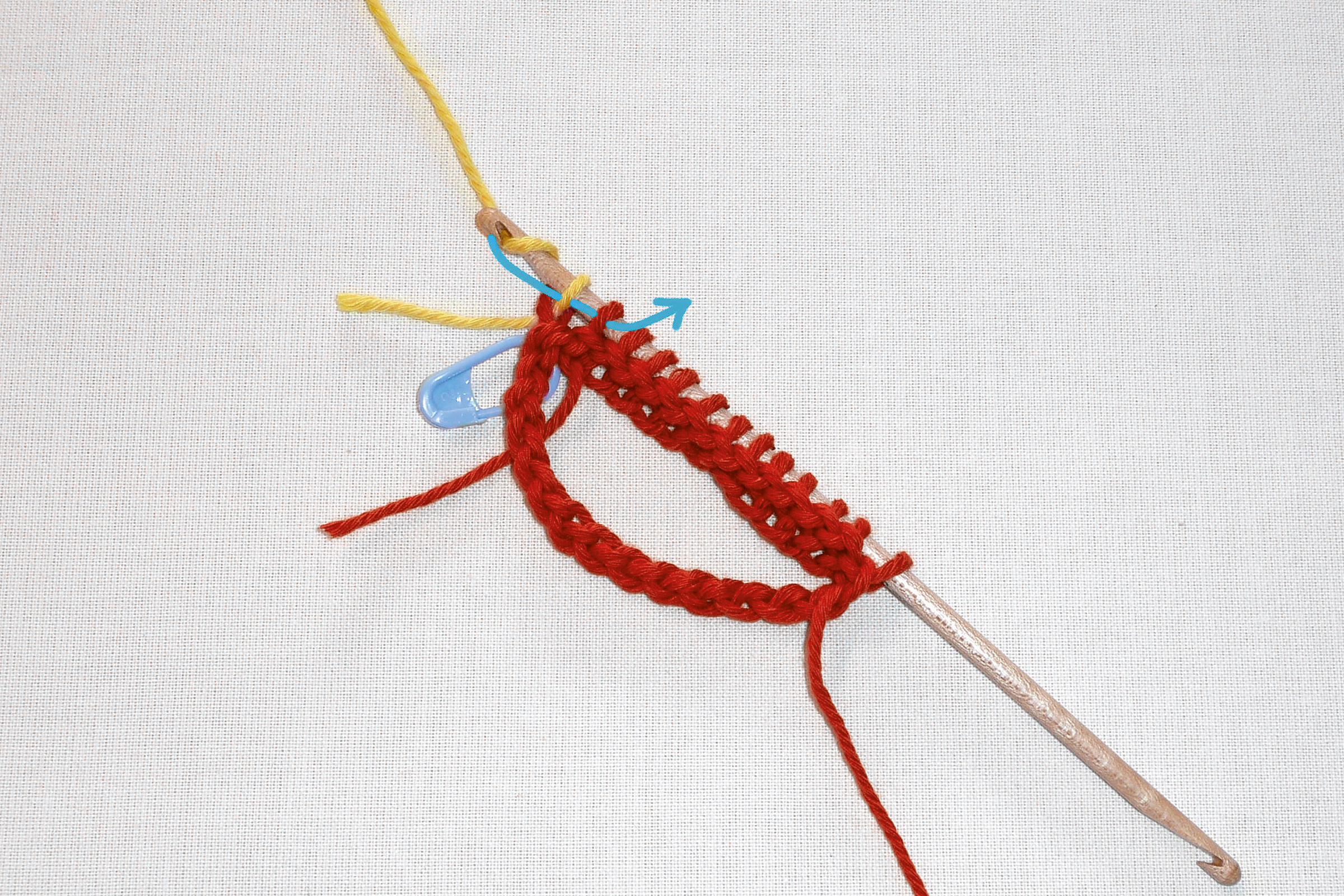 Rote Häkelarbeit an Haken, detailreich und modisch, DIY-Charakter. Farben: Rot, Gelb, Blau.