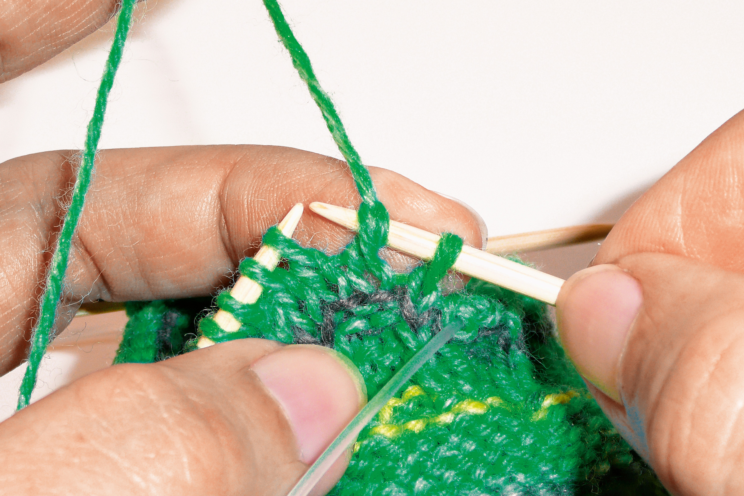 Grünes, handgemachtes Strickmuster mit gelben Akzenten. Fein stricken mit Holznadeln. Kreative Handarbeit.