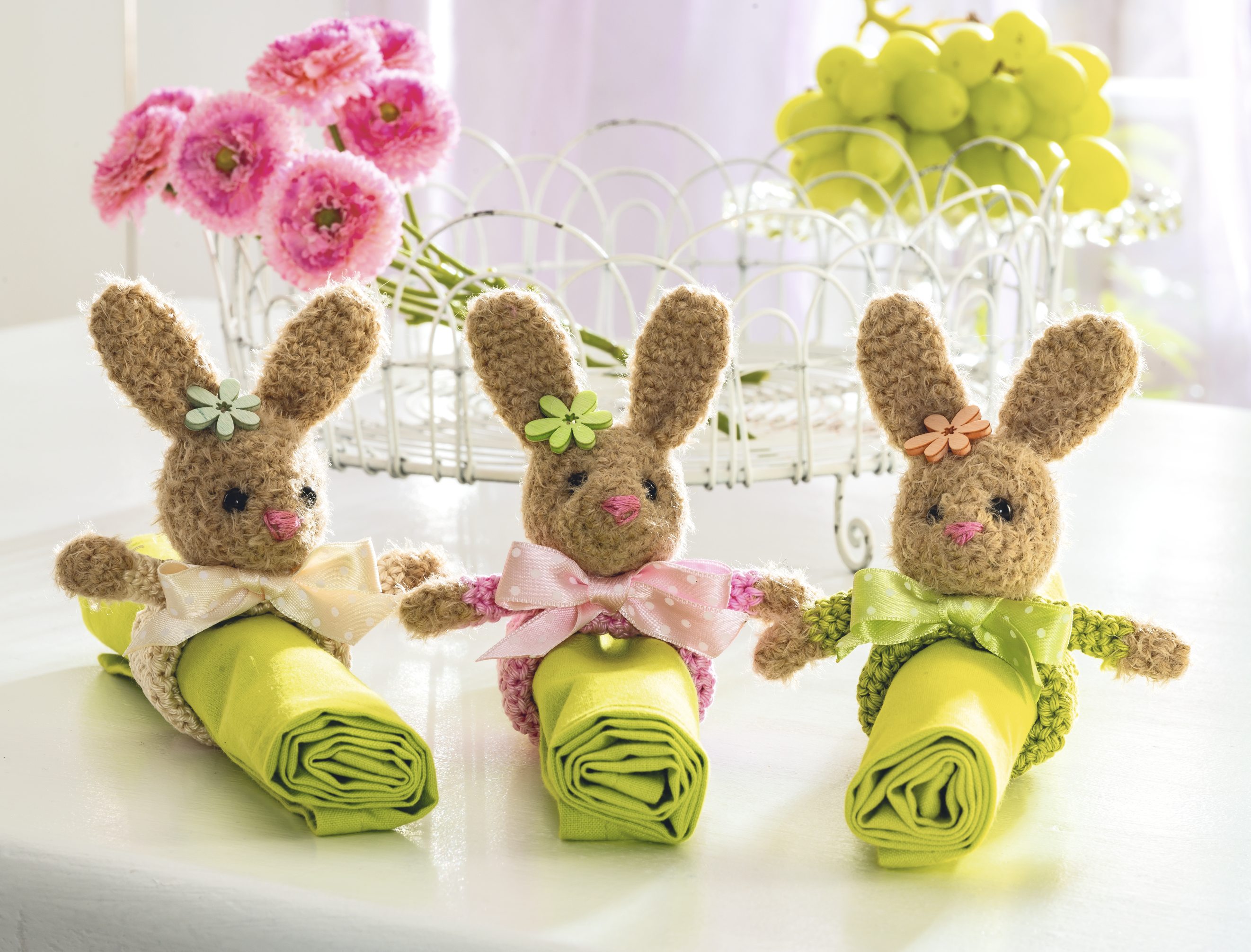 Gestrickte Hasen mit bunten Schleifen und Blumen, modisch, DIY. Akzent in Grün-Tönen.