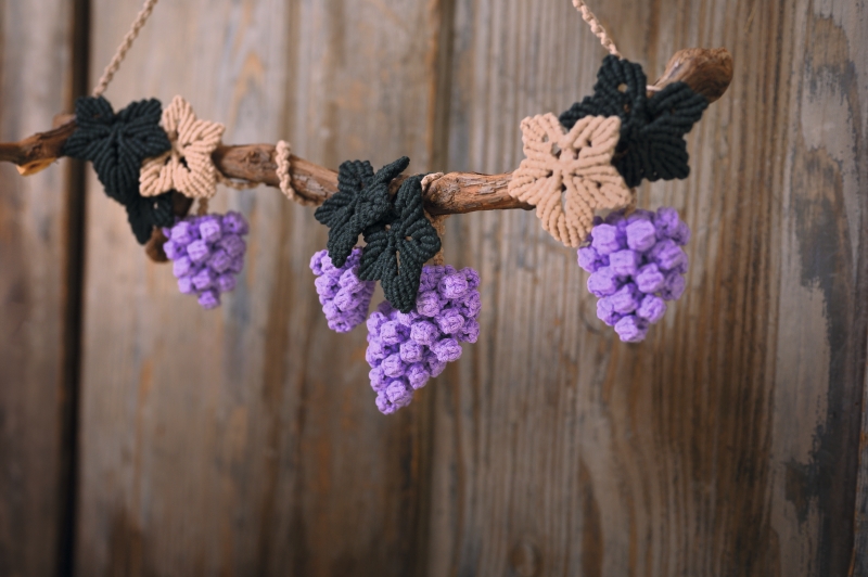 Lila Trauben aus Garn, mit grünen und beigen Blättern, kreativ handgearbeitet, DIY-Stil, rustikaler Charme.