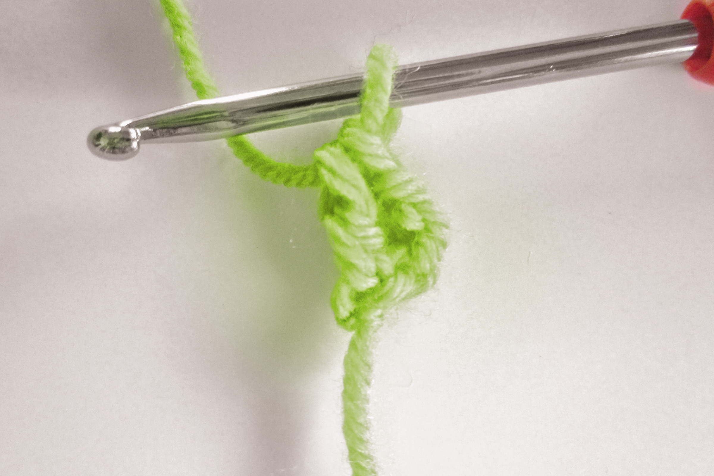 Hellgrüne Häkelarbeit mit glänzender Häkelnadel. Handgemacht, DIY, stilvoll durch lebendige Farbwahl.
