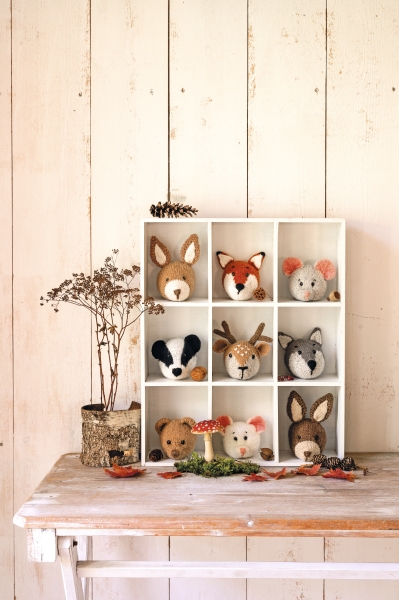 Niedliche, handgefertigte Wolltiere in erdigen Farben, sorgfältig in einem weißen Regal arrangiert.