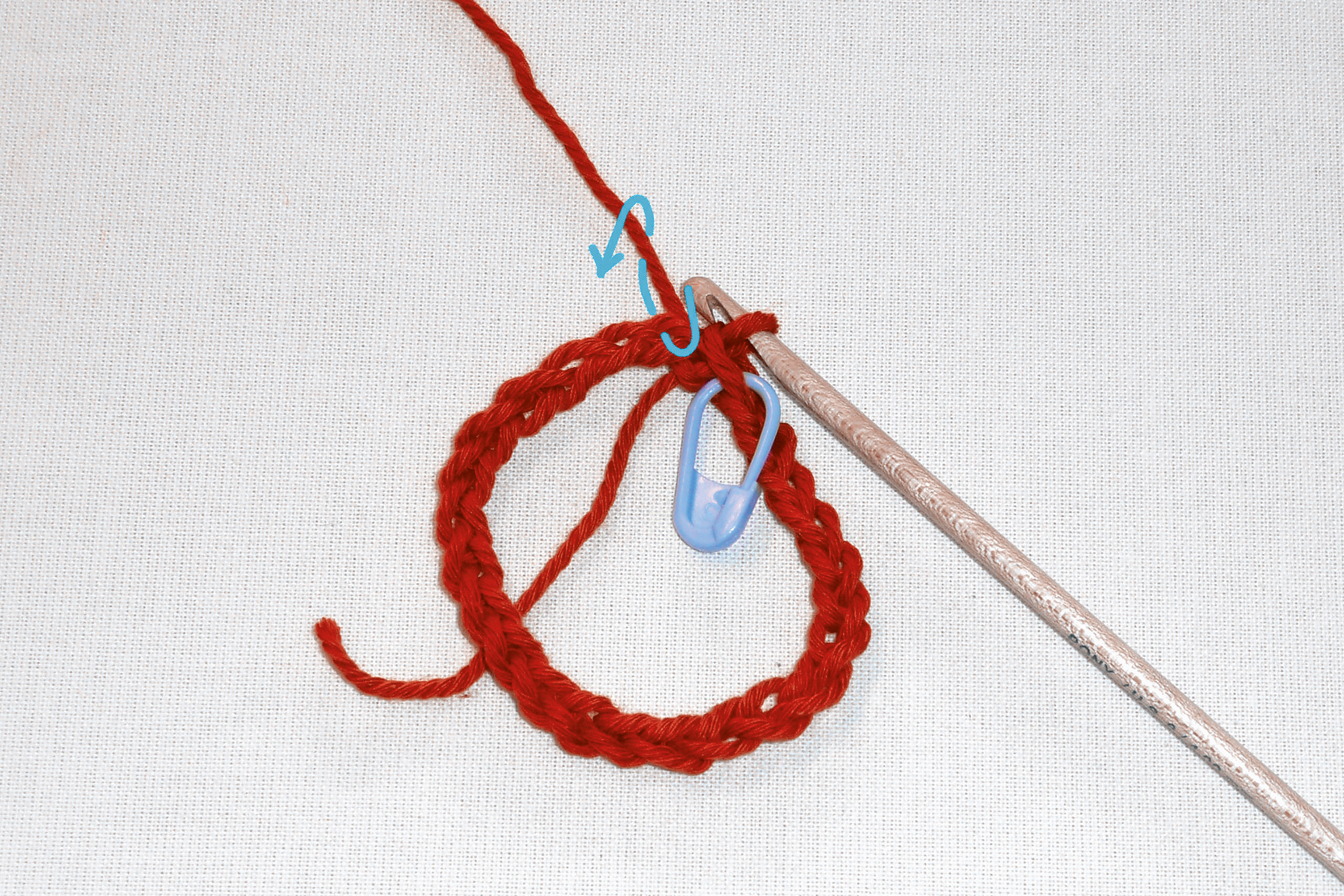 Rote gehäkelte Schlaufe, handgemacht. Häkelnadel und blauer Markierungsstift. Kreative Handarbeit.