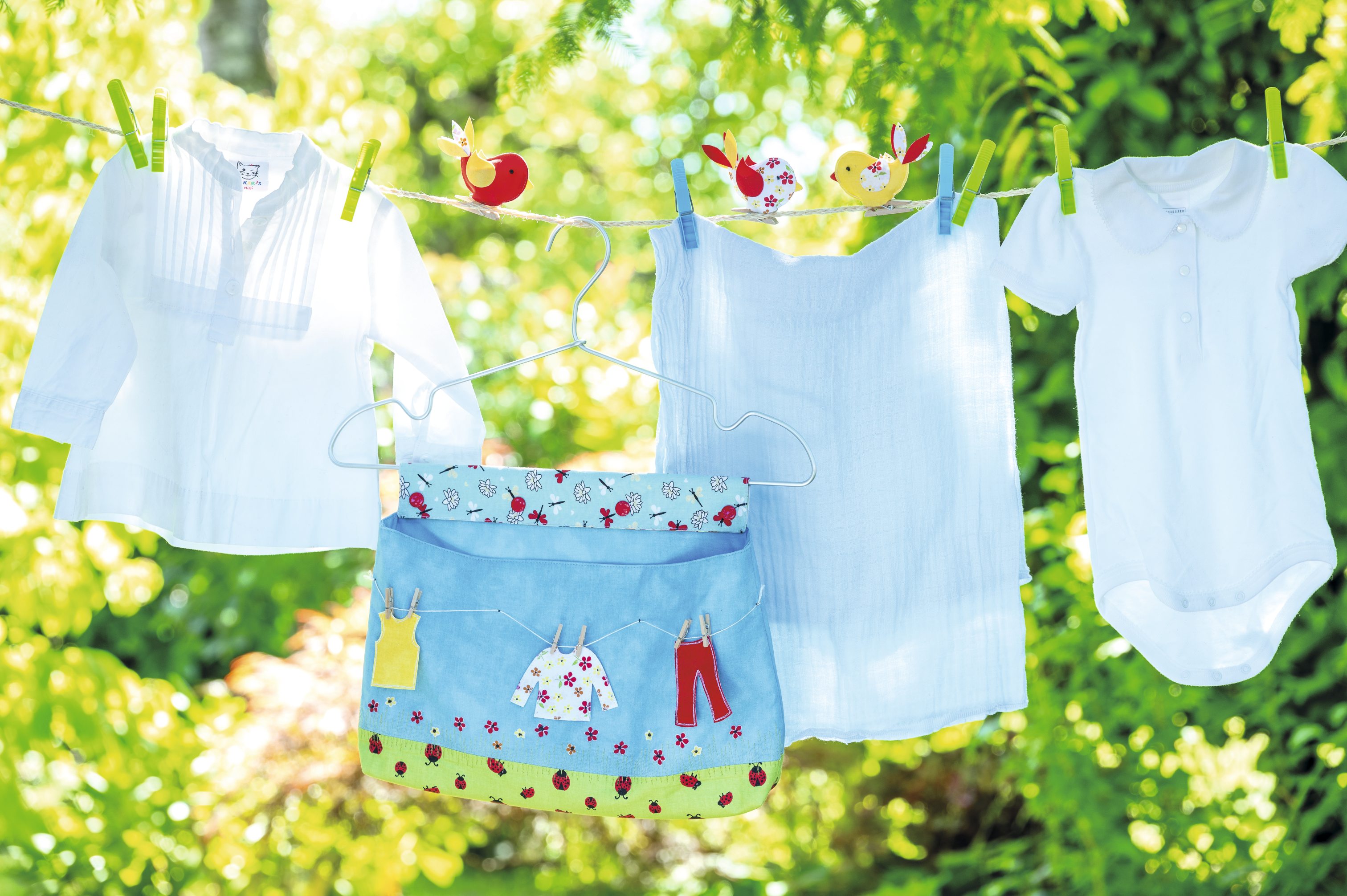 Handgemachte bunte Stofftasche mit kleinem Wäscheprint, fröhliches Muster. Weiße Babykleidung, schlicht und klassisch.