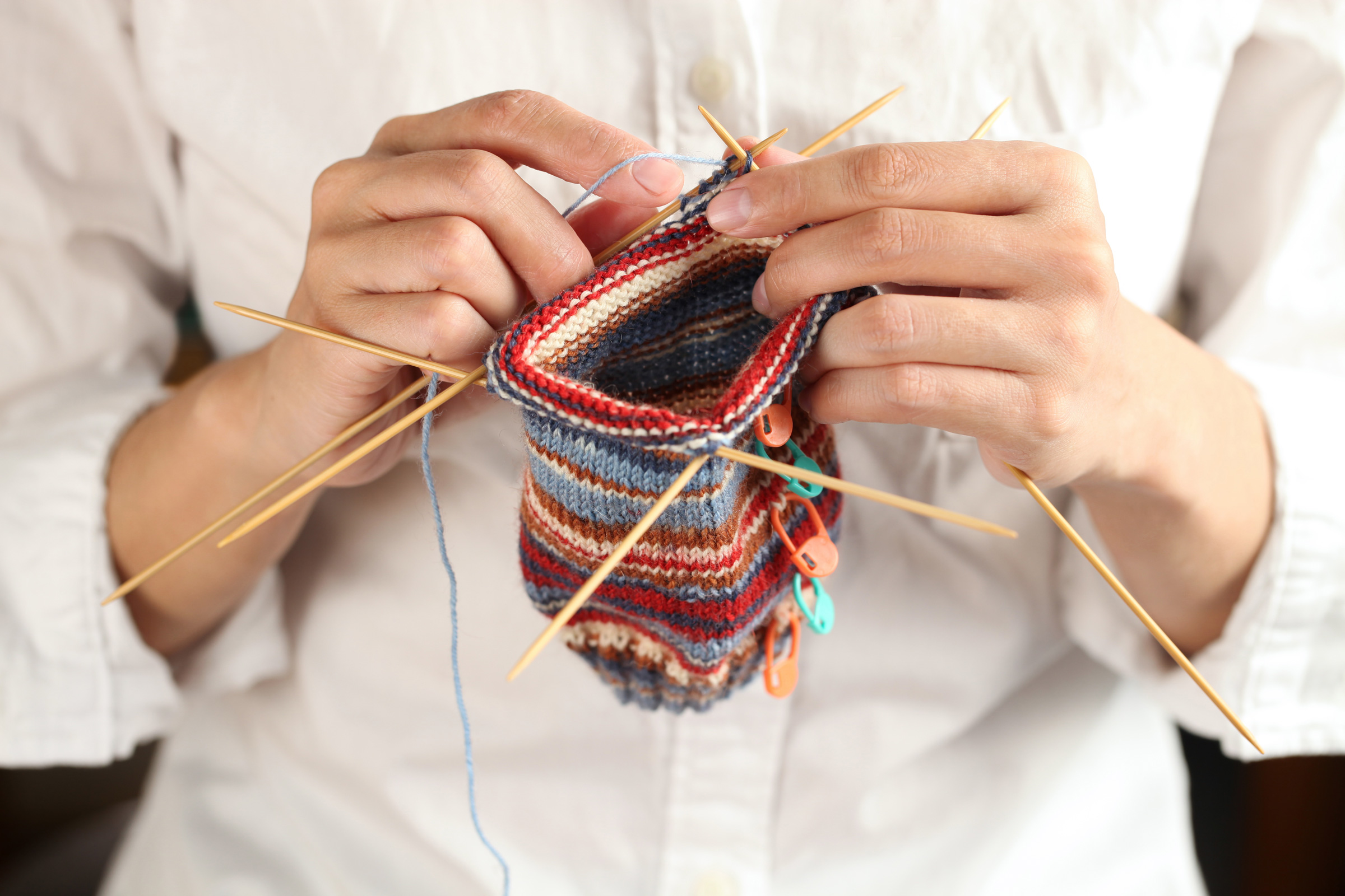 Bunte, gestreifte DIY-Handarbeit mit feinen Nadeln. Modisches, individuelles Muster, kunstvoll gestrickt.