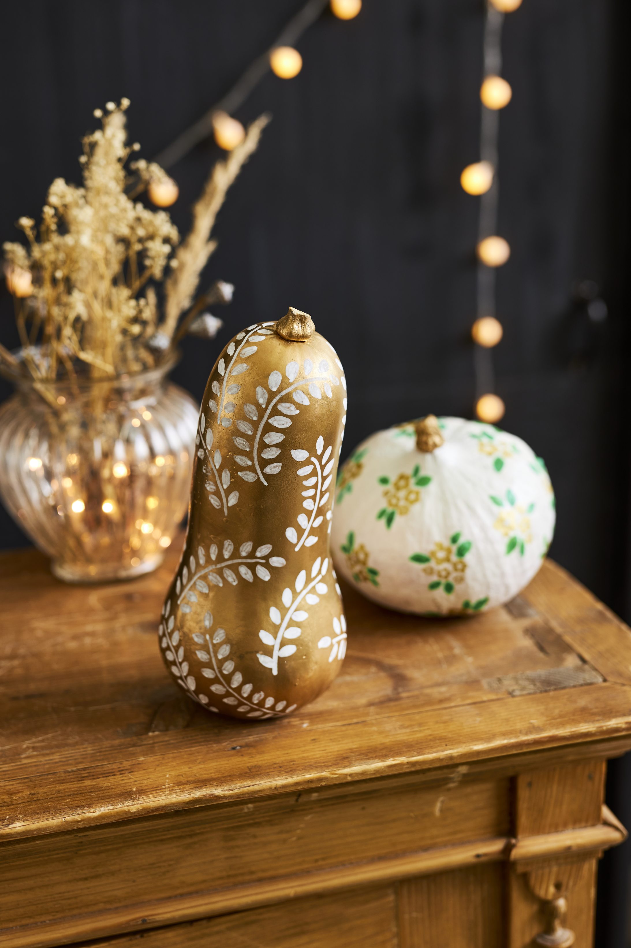 Handbemalte Kürbisse, DIY-Style. Goldbraun mit Blattmustern und weiß mit gelben Blüten. Kreativ und dekorativ.