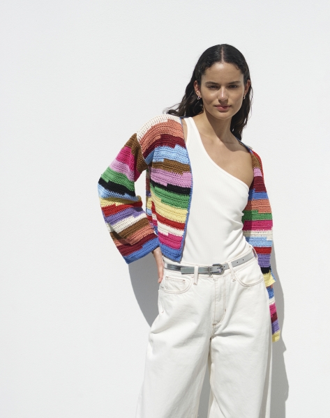 Modische, handgearbeitete Streifenjacke in bunten Farben. Kombiniert mit weißem Top und lockerer Hose.