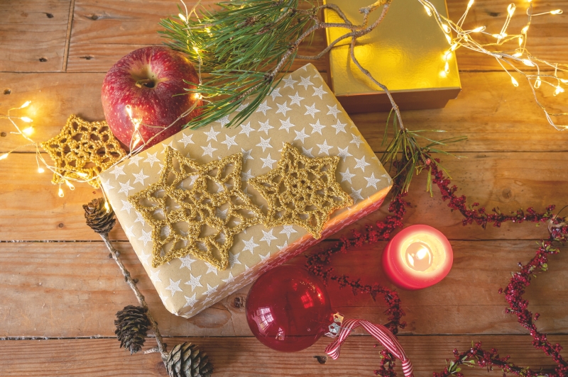 Geschenk verpackt in sternenbedrucktem Papier, verziert mit handgemachten goldenen Häkelsternen. Festlich, DIY.