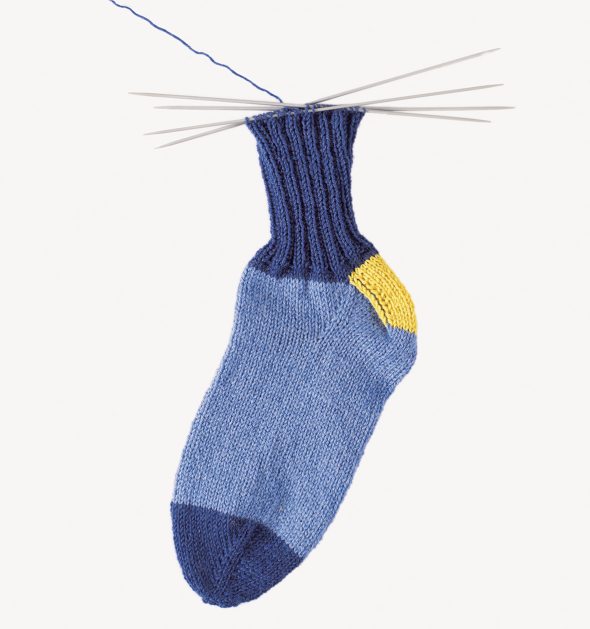 Handgestrickte Socke in Blau mit gelber Ferse. Kreatives DIY-Design, modisch und einzigartig.