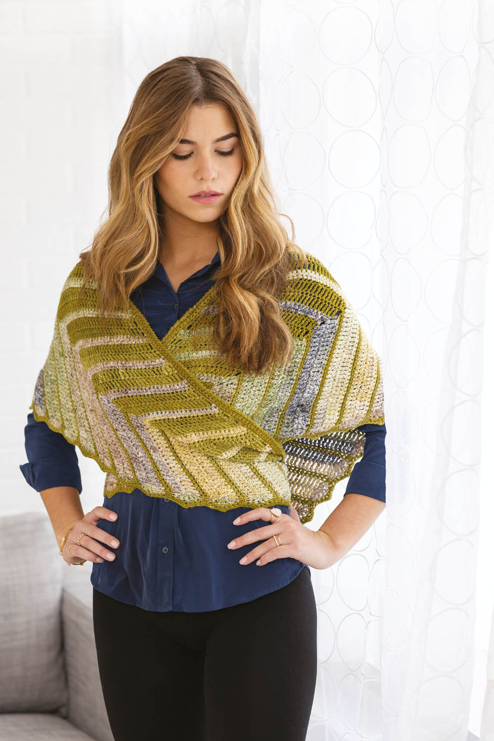 Handgemachter, gestreifter Schal in Grün- und Gelbtönen. Zickzack-Muster, elegant über blauer Bluse getragen.