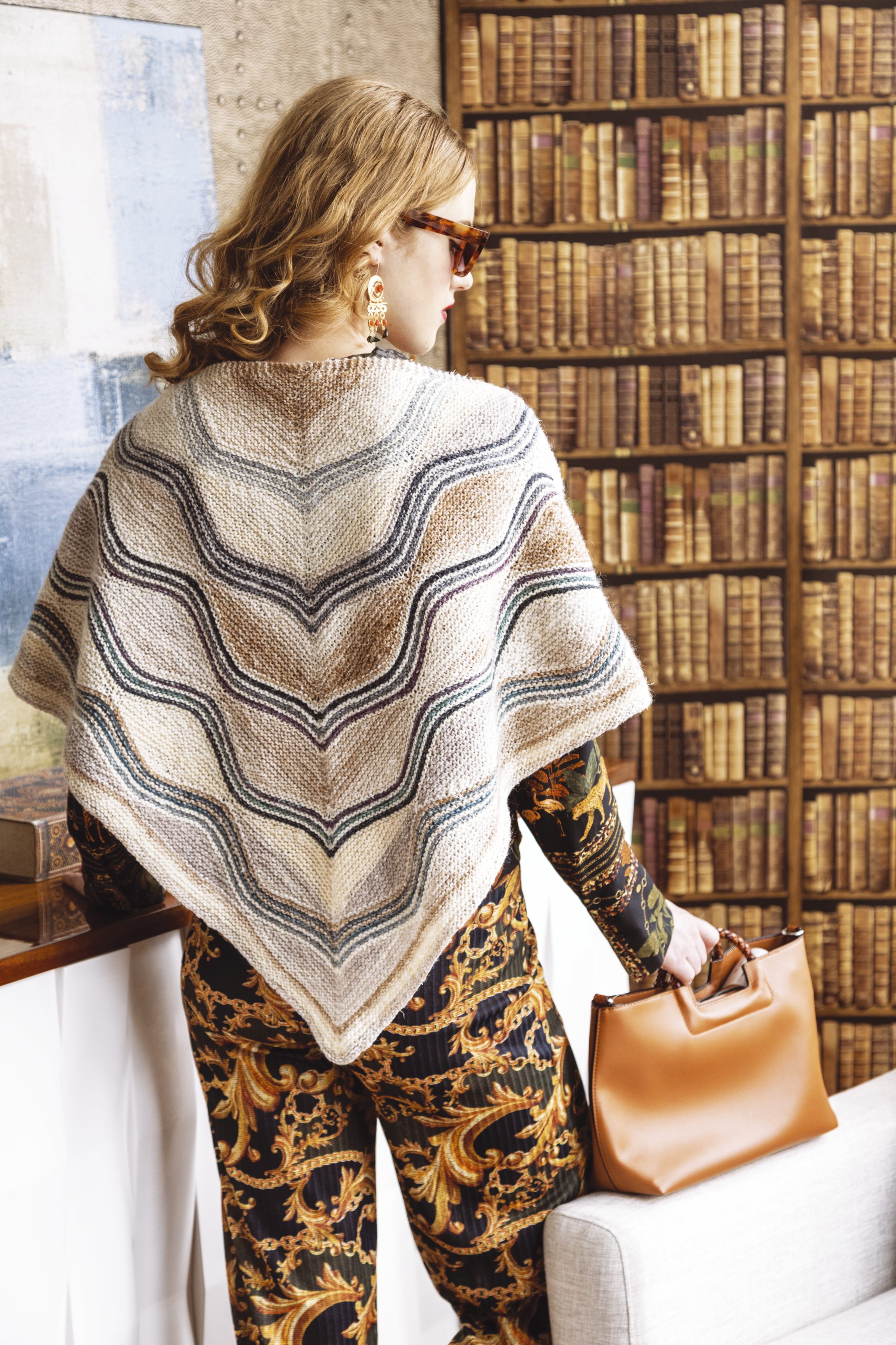 Handgestricktes Cape mit Wellenmuster in warmen Tönen, kombiniert mit elegantem, gemustertem Overall.