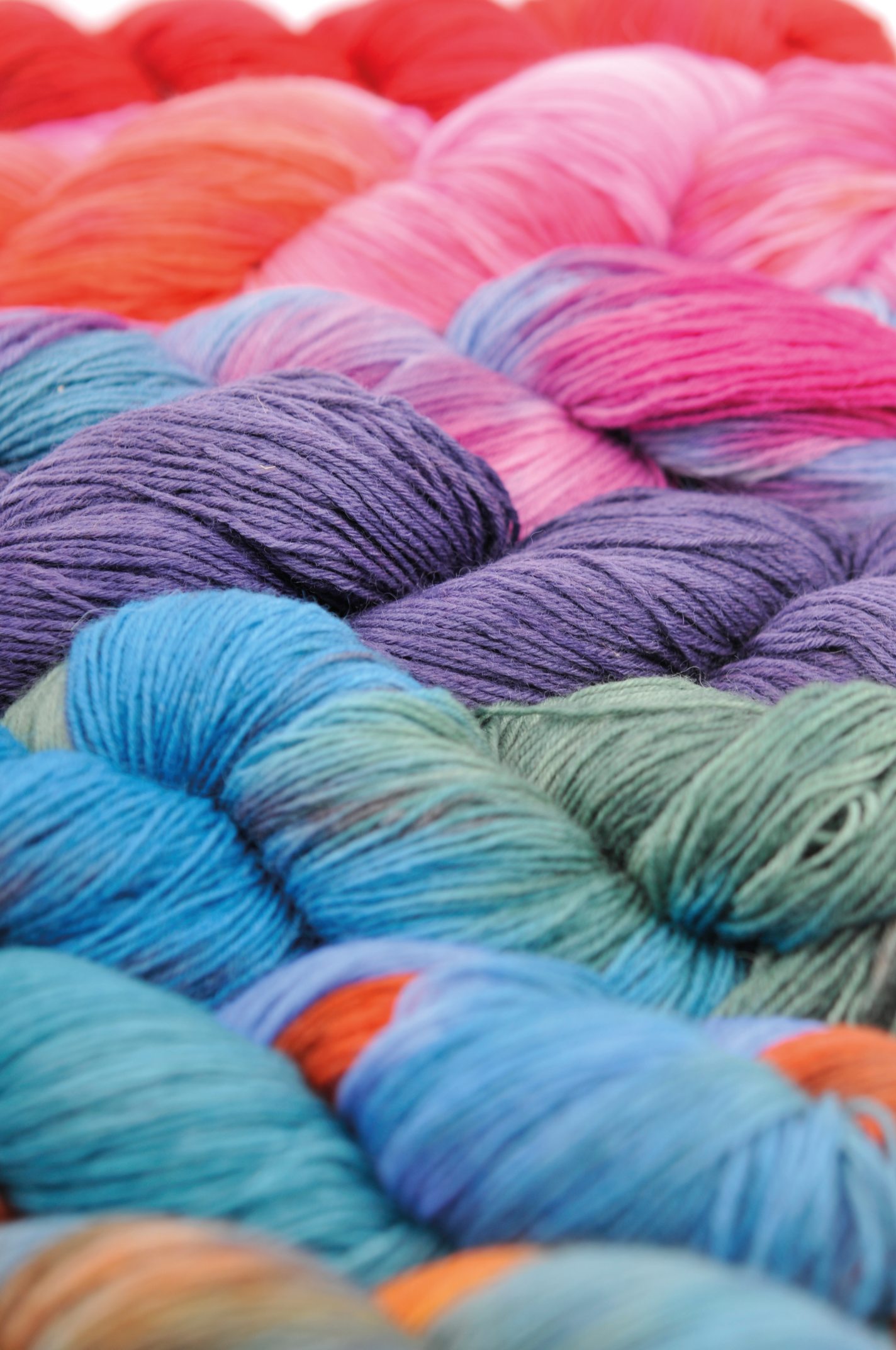 Vielfarbige Garnstränge in Blau, Rosa, Lila und Grün. Perfekt für modisch-handgemachte DIY-Projekte.