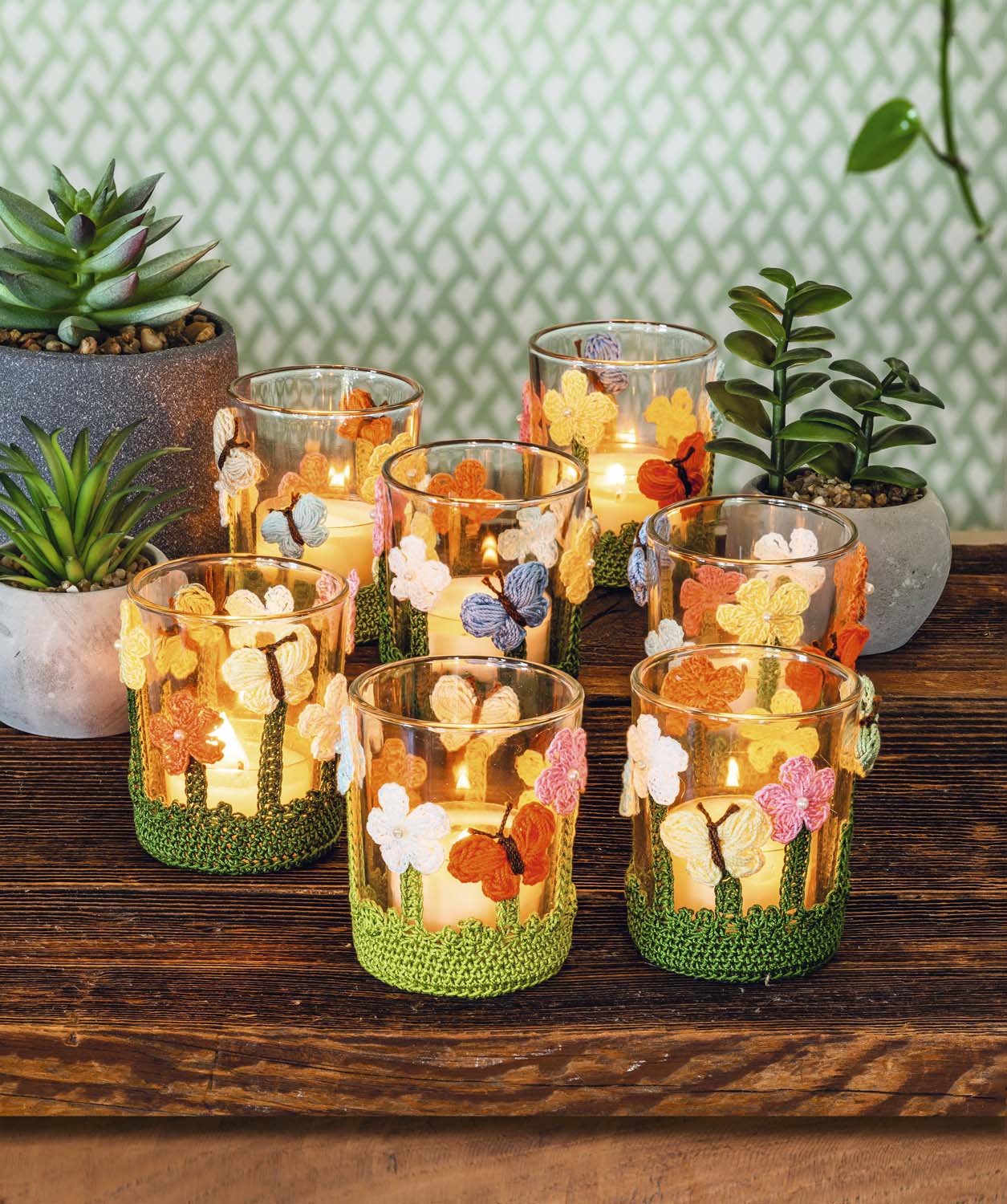 Kerzengläser mit bunt gehäkelten Blumenmustern. Modisch, handgemacht, DIY-Stil, grüne Basis.