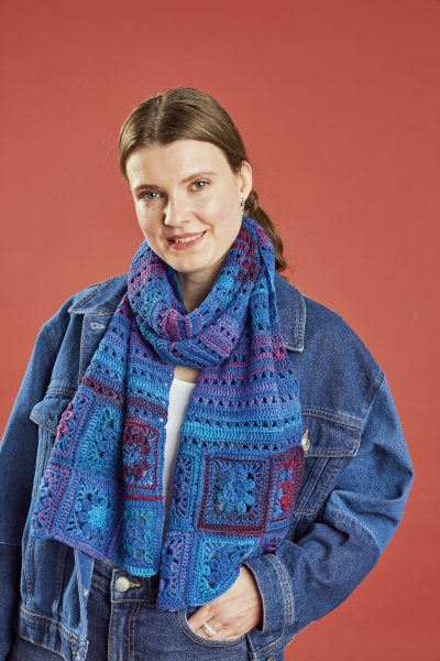Bunter Patchwork-Schal in Blau-Lila, modisch, grobe Strickmuster, über Denimjacke getragen.