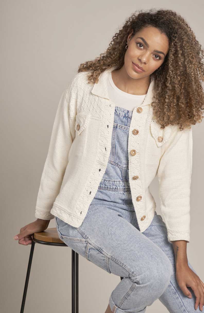 Cremefarbene handgemachte Jacke mit Holzknöpfen über hellblauem Jeans-Overall. Modisch, zeitlos, entspannt.
