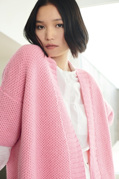 Rosa grob gestrickter Cardigan, locker geschnitten, über weißem Oberteil. Modern, handgemacht, stilvoll.