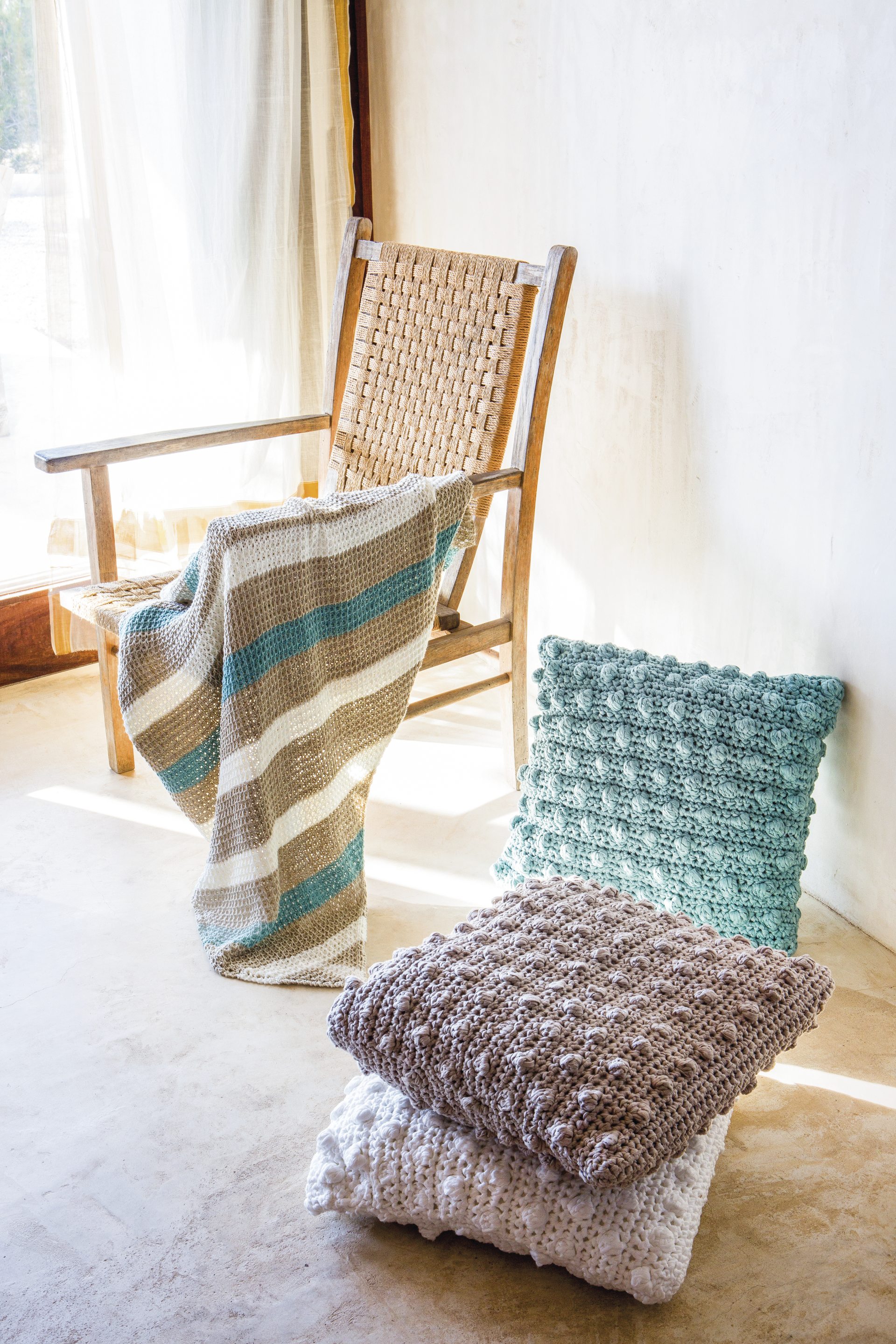 Modisch, handgemachte Kissen in Strickoptik, sanfte Farben; Decke mit Streifenmuster in Beige, Blau und Weiß.