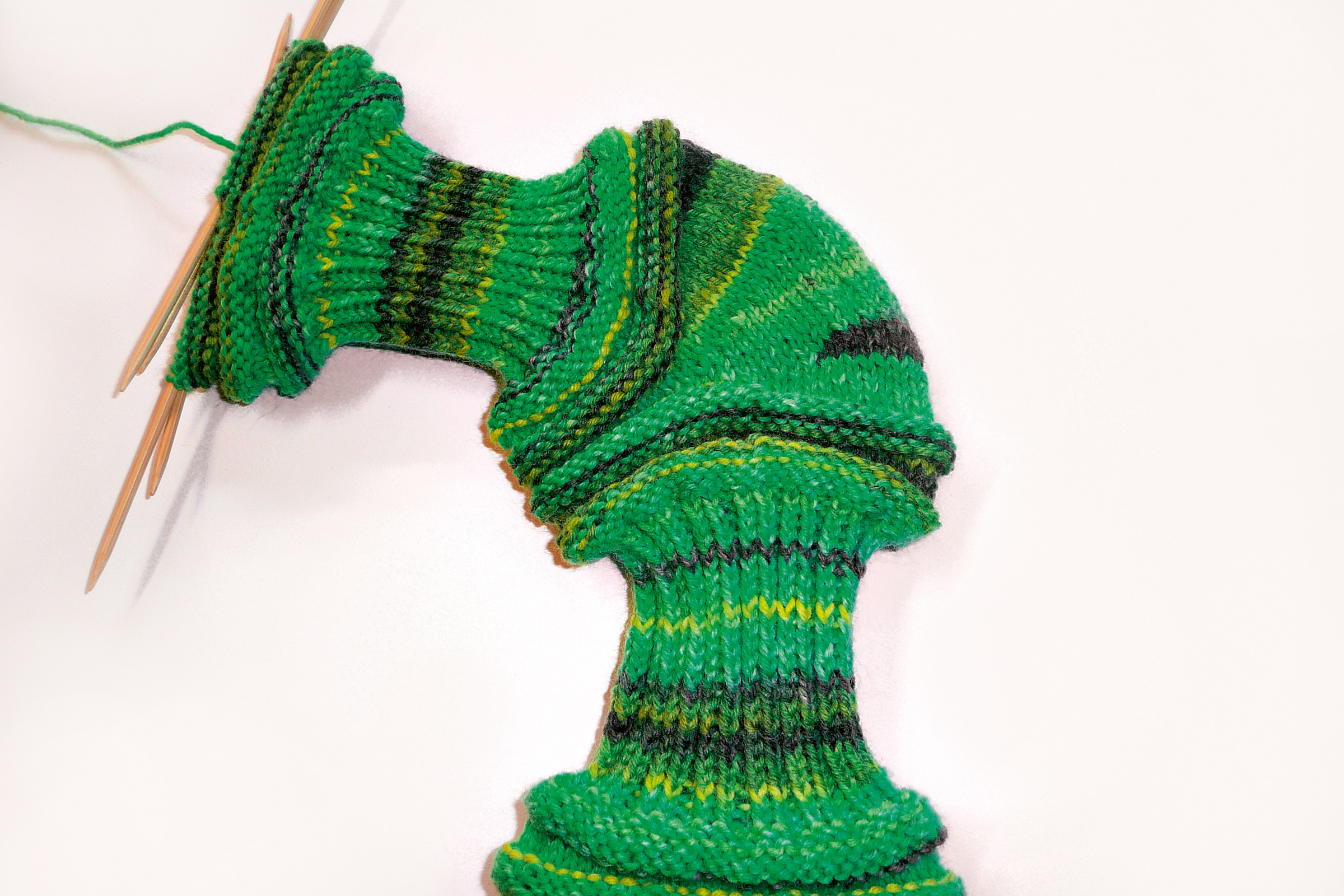 Modisches, handgemachtes Strickstück in grünen Farbtönen, mit variierenden Streifenmustern und markanten Rundungen.