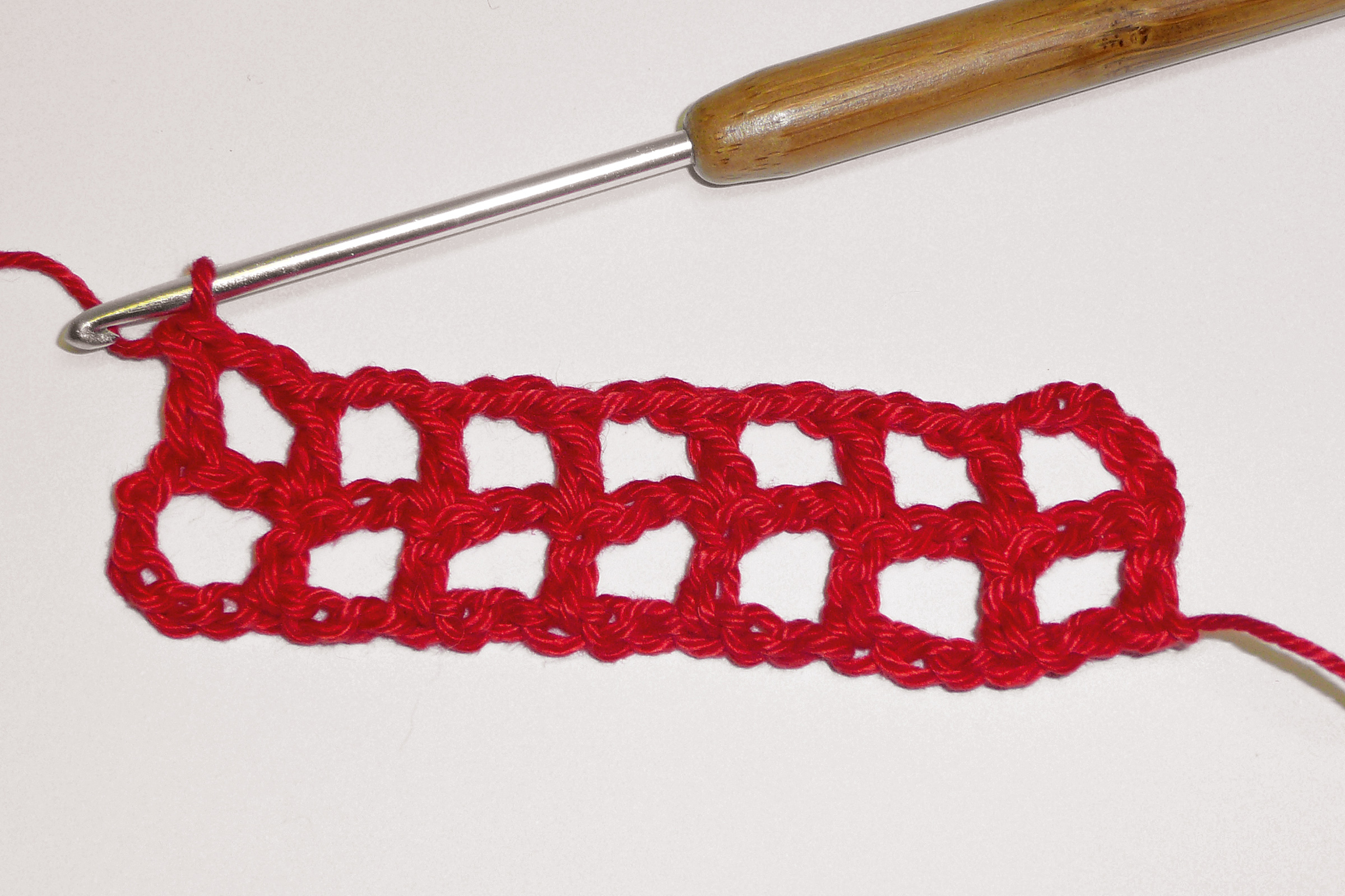 Leuchtend rotes, handgemachtes Häkelmuster. Gitteroptik, quadratisch, DIY-Charme. Kreativ und lebendig.