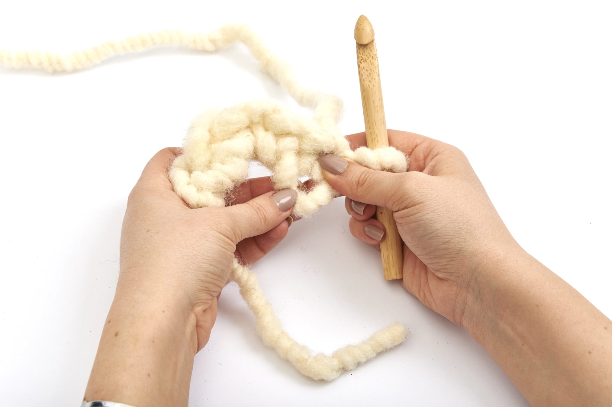 DIY Strickprojekt mit grobem, cremefarbenem Garn; dicke Maschen, massive Holzstricknadel. Handgemacht.
