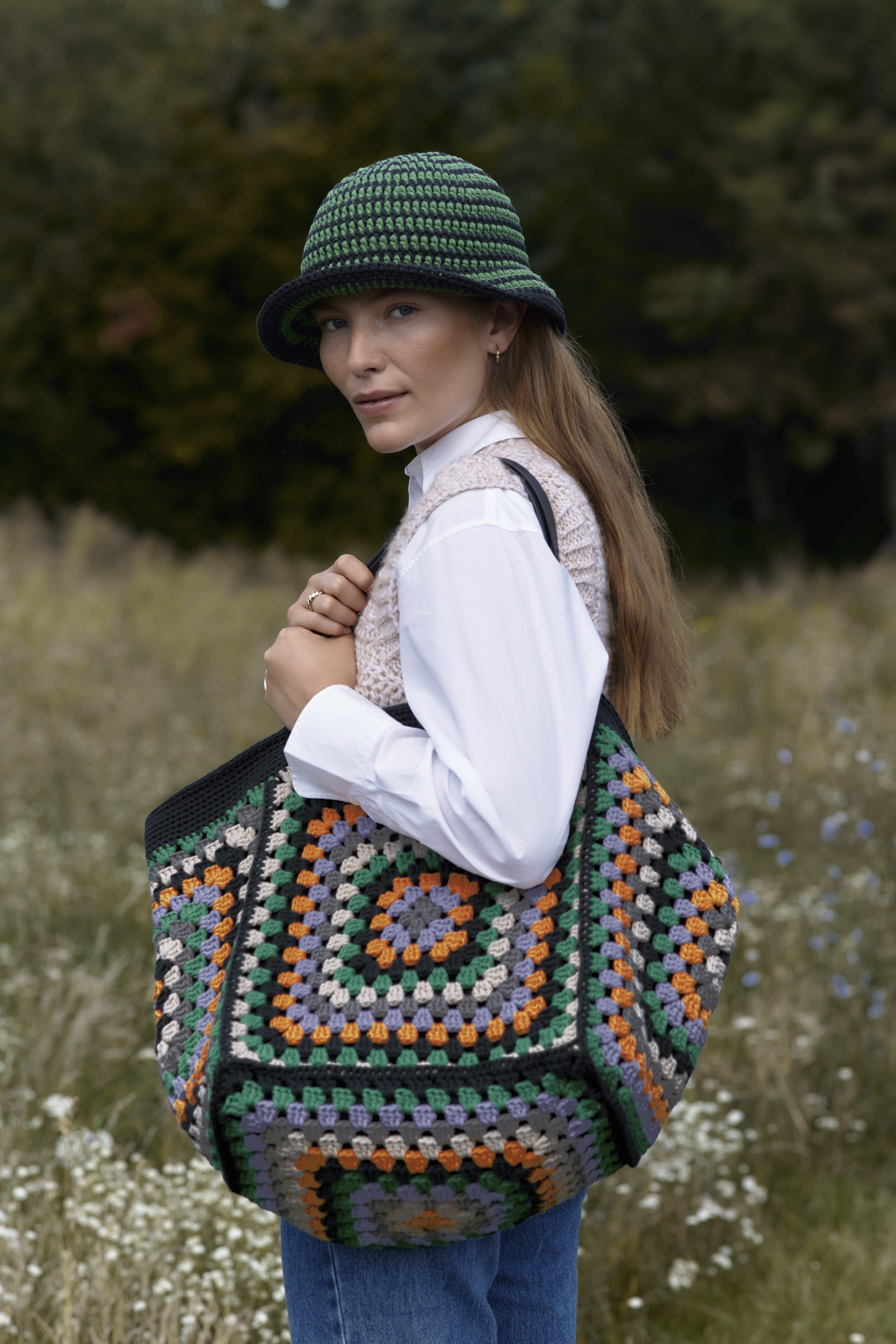 Grüner Häkelhut, gemusterte DIY-Tasche, bunte Quadrate, modisch, handgearbeitet, weißes Hemd, lässiger Stil.