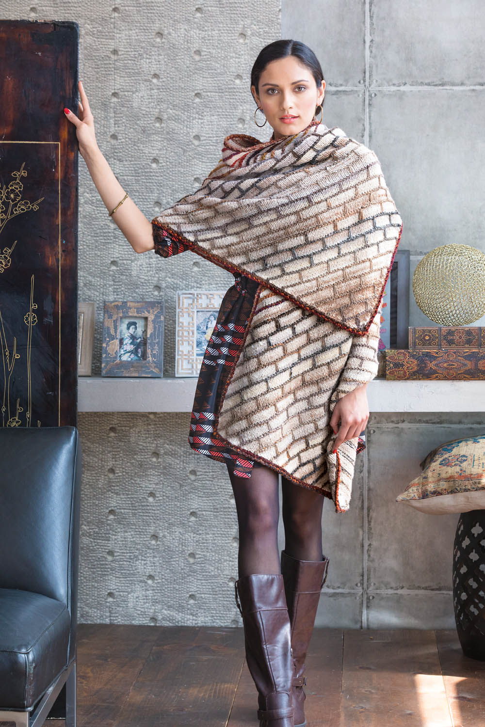 Beiger Poncho mit Ziegelmuster, rot gesäumt, kombiniert mit braunen Stiefeln. Modisch und handgearbeitet.