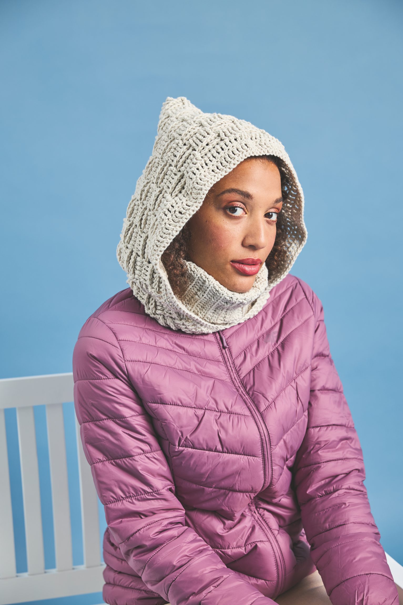 Modische Strickkapuze mit Zopfmuster, kombiniert mit purpurfarbener Steppjacke. Handarbeit, DIY-Charme.