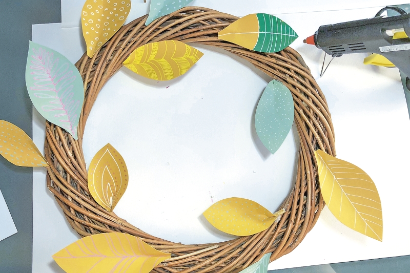 Geflochtener Kranz mit bunten Papierblättern in Gelb und Grün. DIY, handwerklich, saisonal dekoriert.