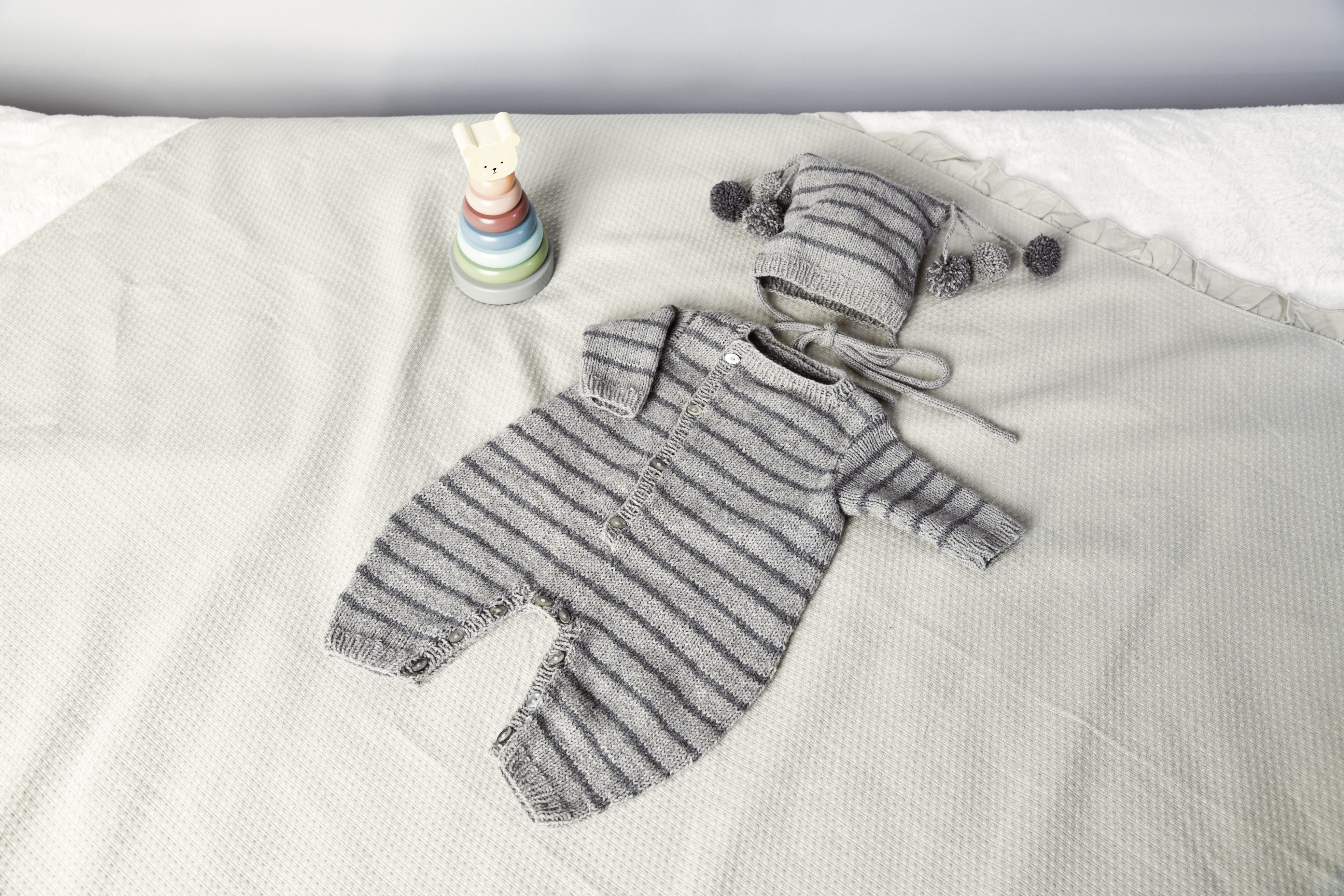 Grau-gestreifter Babystrampler mit Pom-Pom-Mütze, handgemacht, gemütlich, stilvoll, DIY.