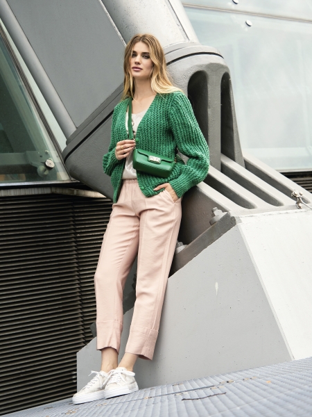 Grüner, handgemachter Pullover, rosa Hose, weiße Sneaker. Modisch und lässig kombiniert.