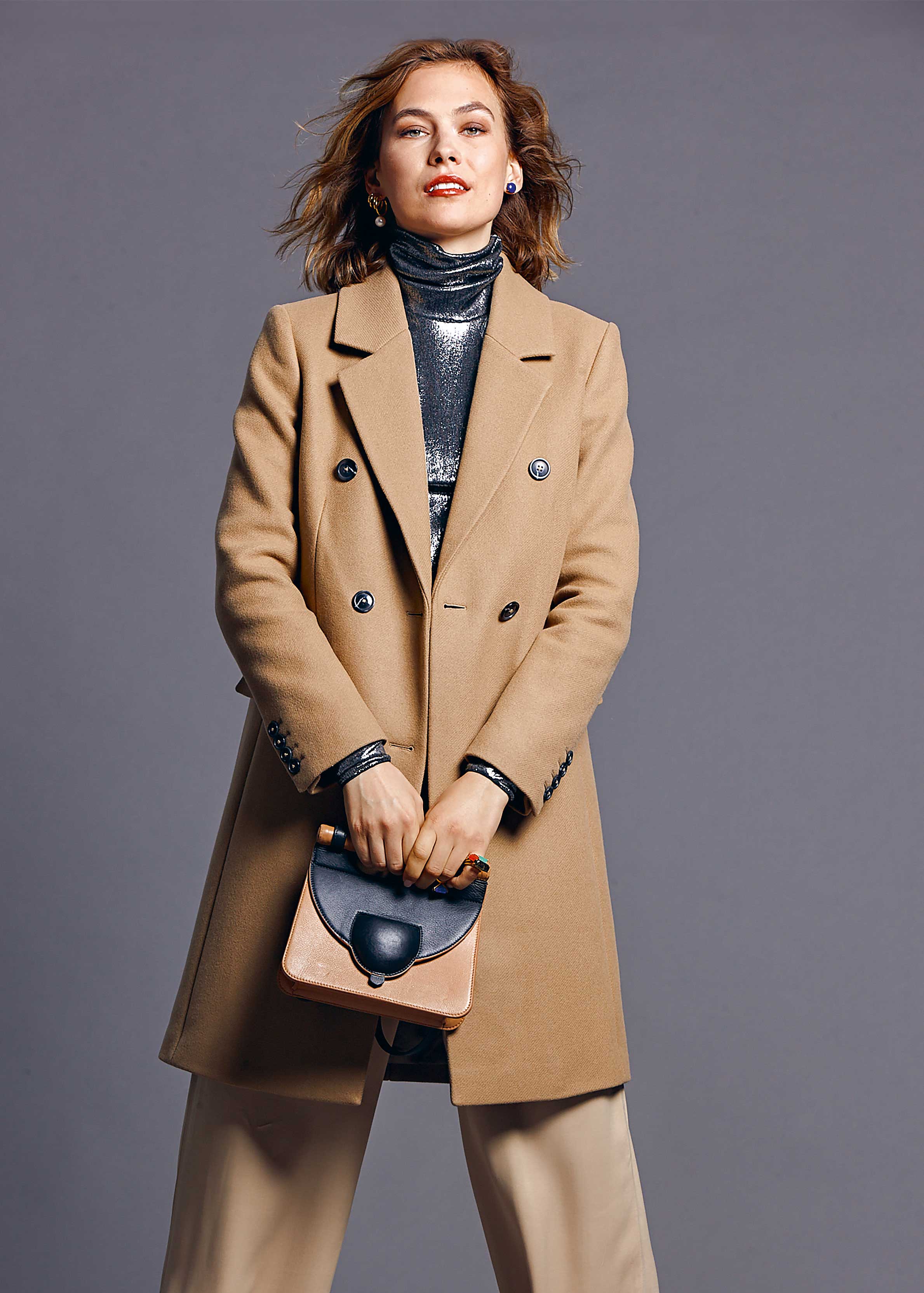 Kamelmantel, doppelreihig, mit Schimmer-Rollkragen, schlichte Hose, schicke Tasche. Modisch, zeitlos.