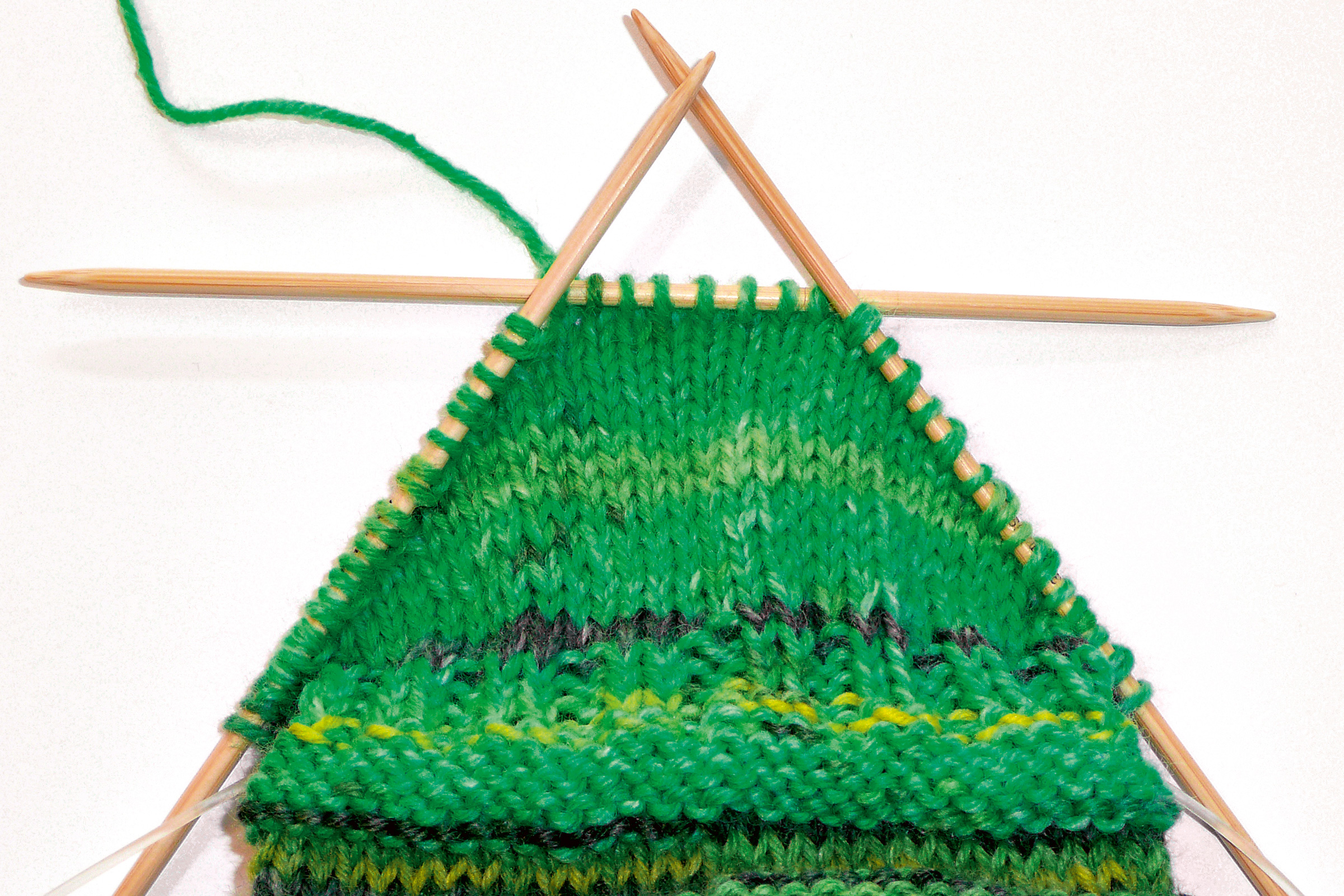 Handgearbeitetes Strickwerk in grünen Farbtönen, gemustert, mit Holznadeln. DIY, modisch.