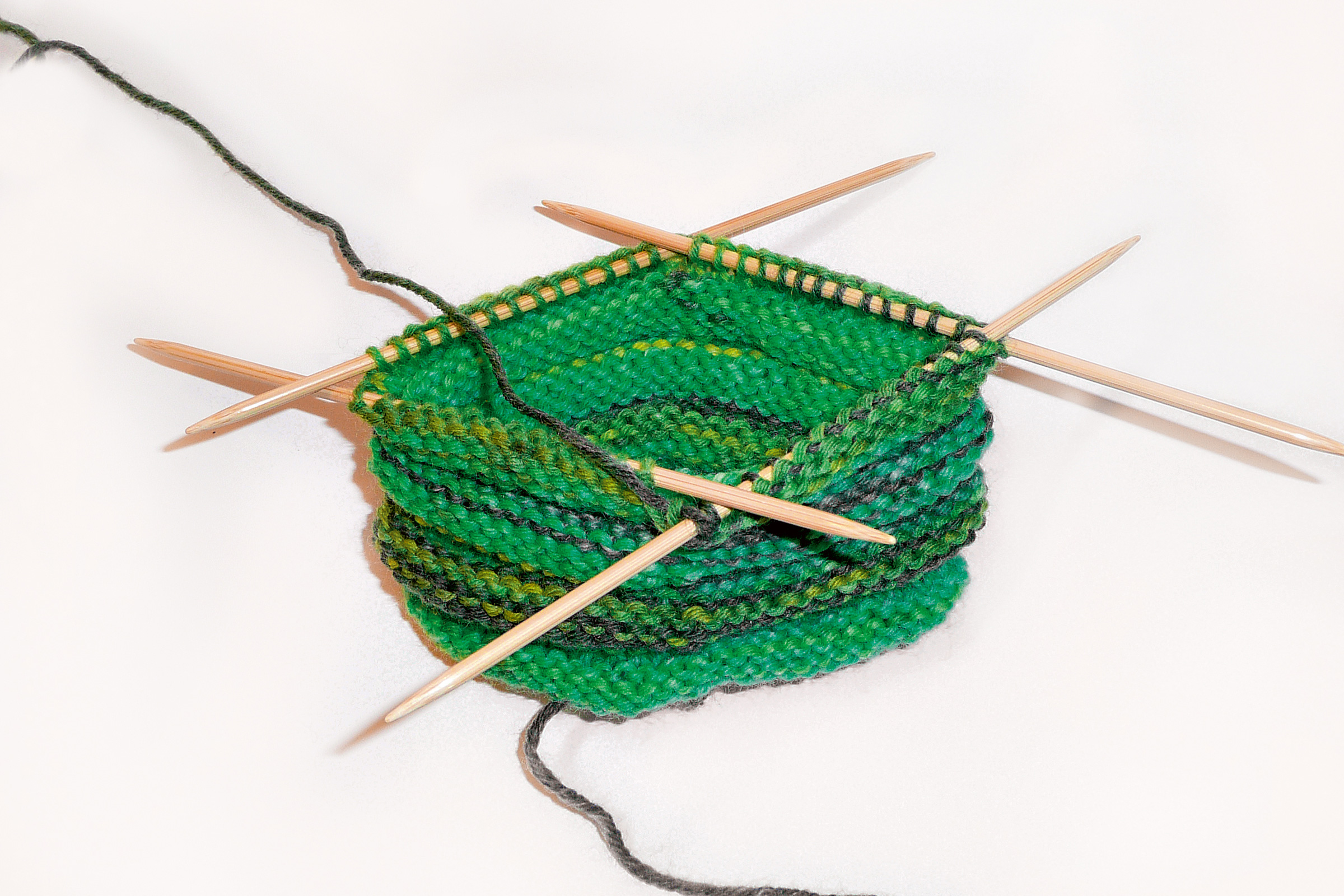Grünes, handgestricktes Projekt mit mehrfarbigem Garn. Holzstricknadeln, DIY-Charme, modisch und detailreich.