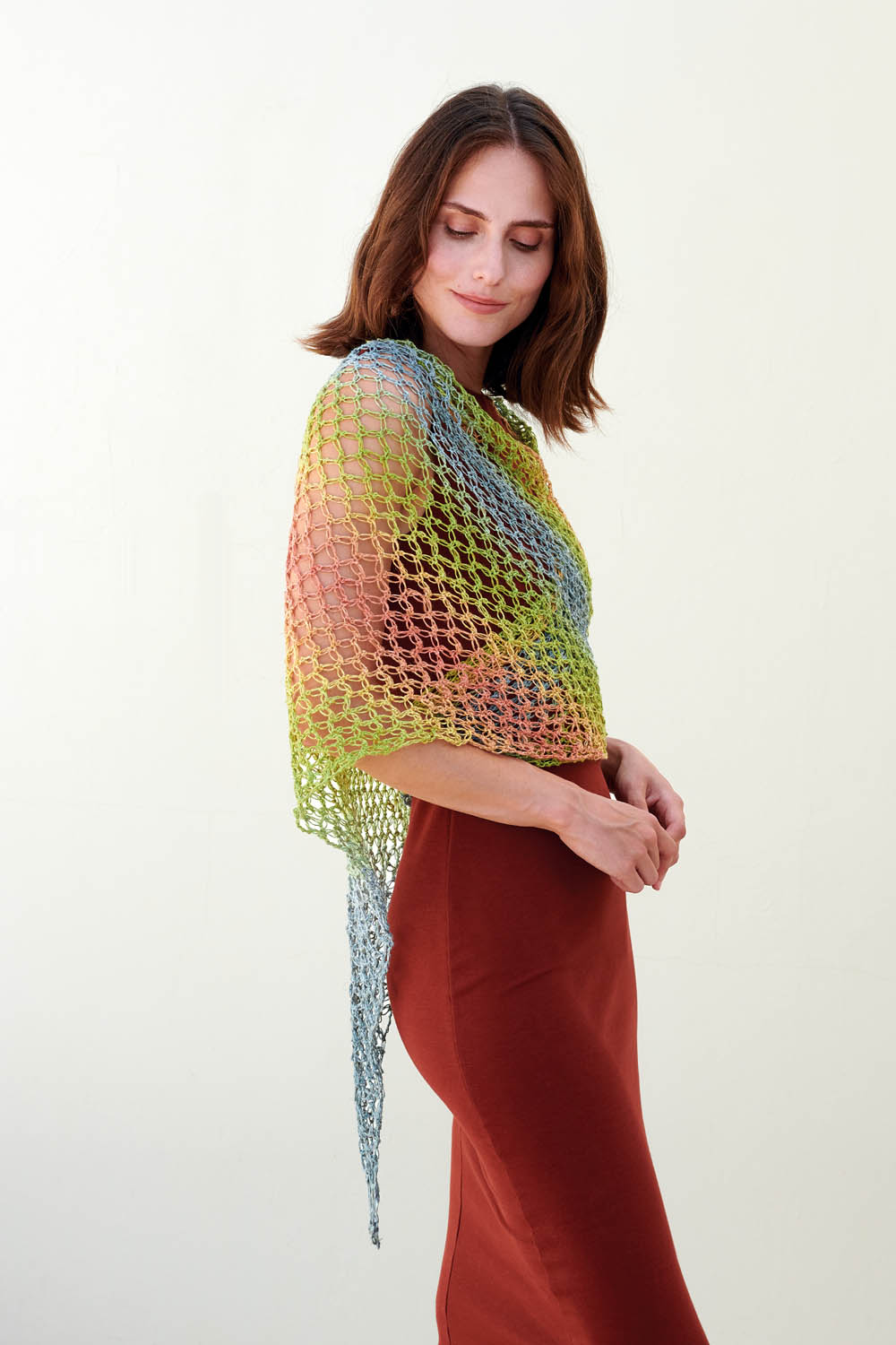 Modisches, handgemachtes, transparentes Häkel-Tuch in Regenbogenfarben auf einem rotbraunen Kleid.