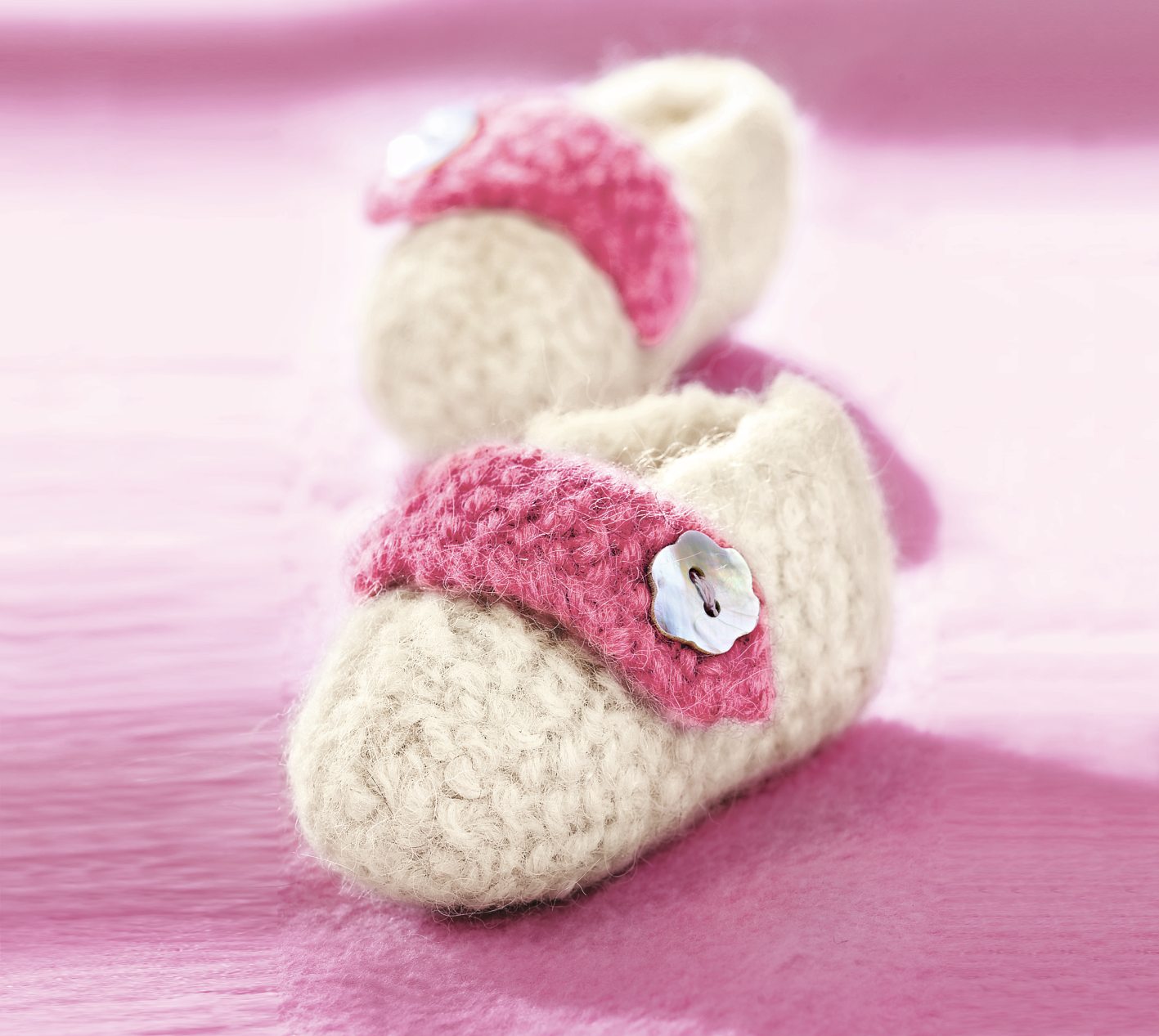 Handgemachte cremeweiße Booties mit rosa Knopf. Flauschiges Garn, stilvoll, DIY, modisch.