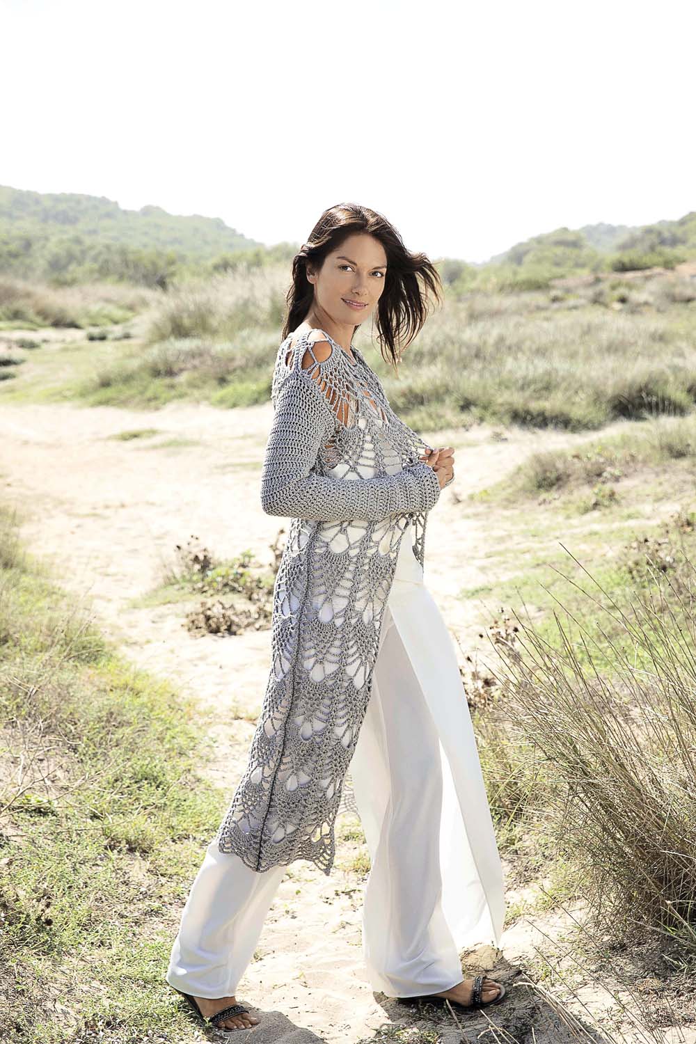 Grauer, handgemachter Strickmantel mit Häkelmuster, kombiniert mit weißen, weiten Hosen. Modisch und schick.