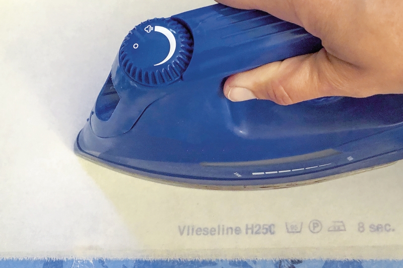 Blaues Bügeleisen auf Vlieseline. DIY-Mode, handgemacht, präzise Arbeit mit angenehmer Farbgestaltung.