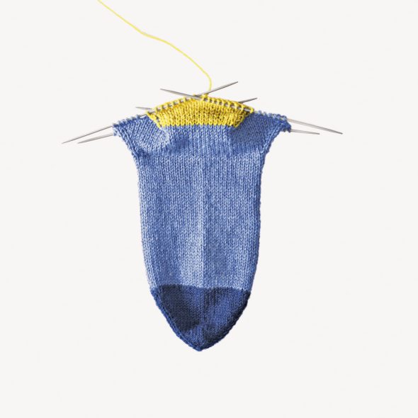 Handgemachte Socke in Blau mit gelbem Akzent, glatt gestrickt, modischer Stil, einzigartiges Design.