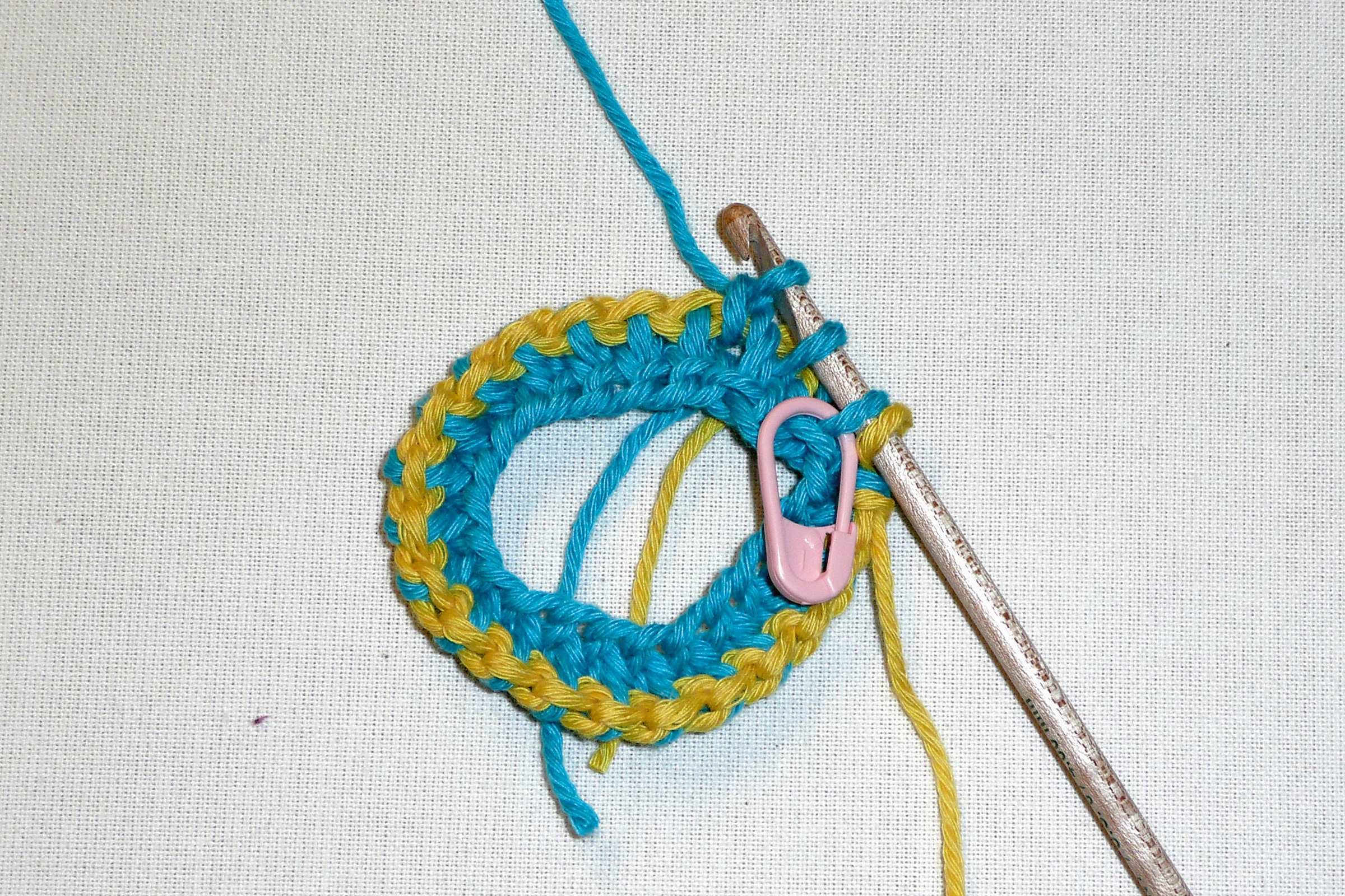 Rundes DIY-Häkelstück, leuchtend blau-gelbe Farben, mit rosa Markierung, modisch und von Hand gemacht.