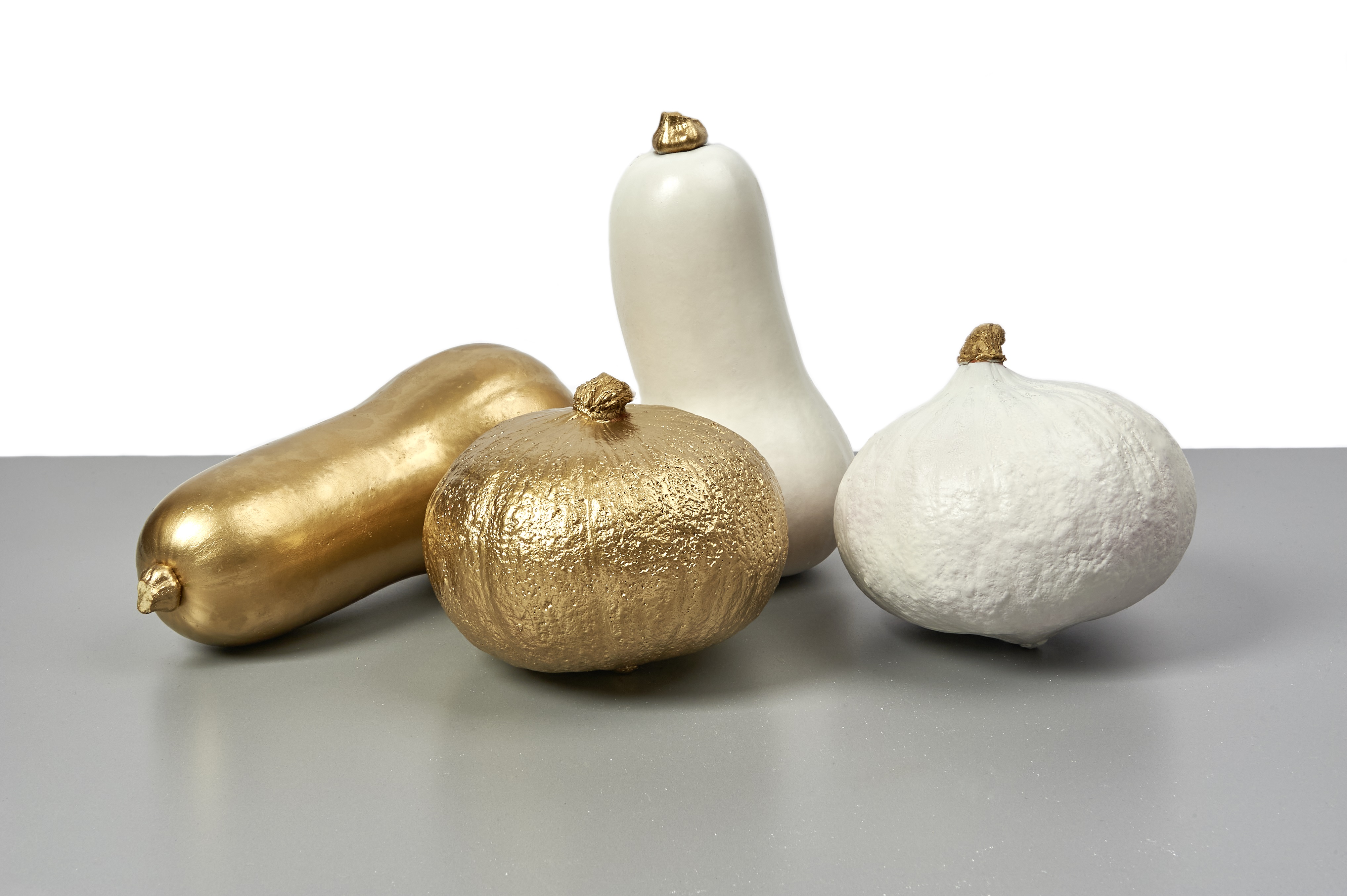 Kürbisse in Gold und Weiß; schimmernde, matte Oberflächen; stilvoll, kunsthandwerklich, dekorativ.