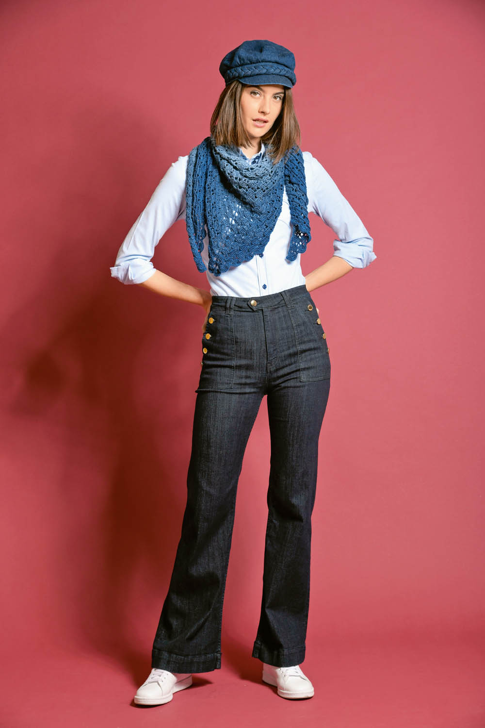 Modische blaue Mütze, gehäkelter Schal, hellbluse, hochgeschnittene Jeans mit Knöpfen, Sneaker. Retro, handgemacht.
