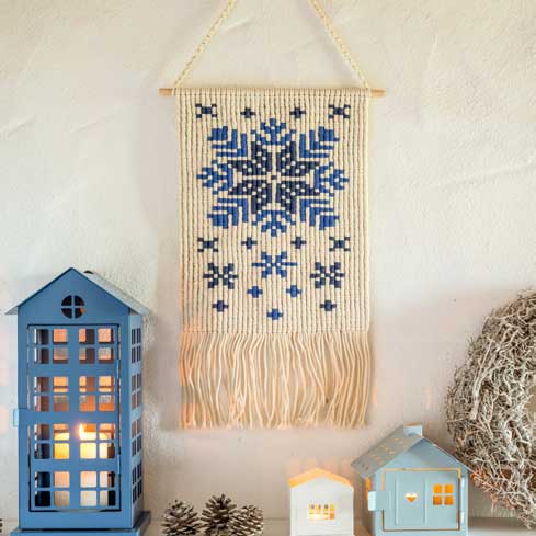 Handgemachtes Wanddekor mit blauen, schneeflockenartigen Mustern und Fransen; DIY-Ästhetik.