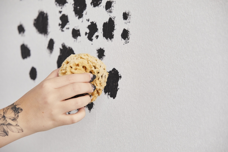 Hand trägt handgemaltes, schwarzes Fleckenmuster auf mit DIY-Technik; kreativ, individuell, modisch.